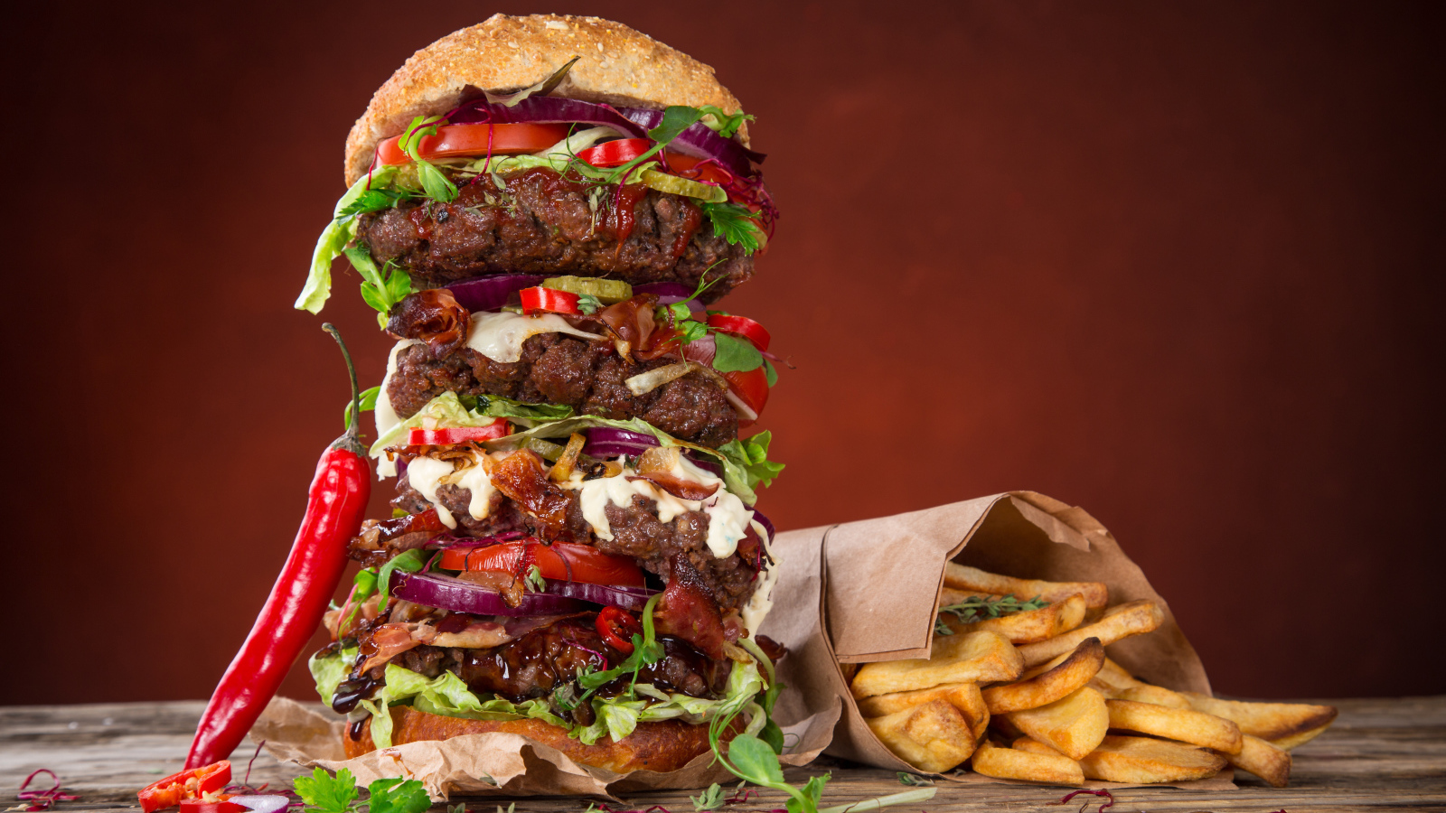 Огромный гамбургер на столе с картофелем фри и острым перцем