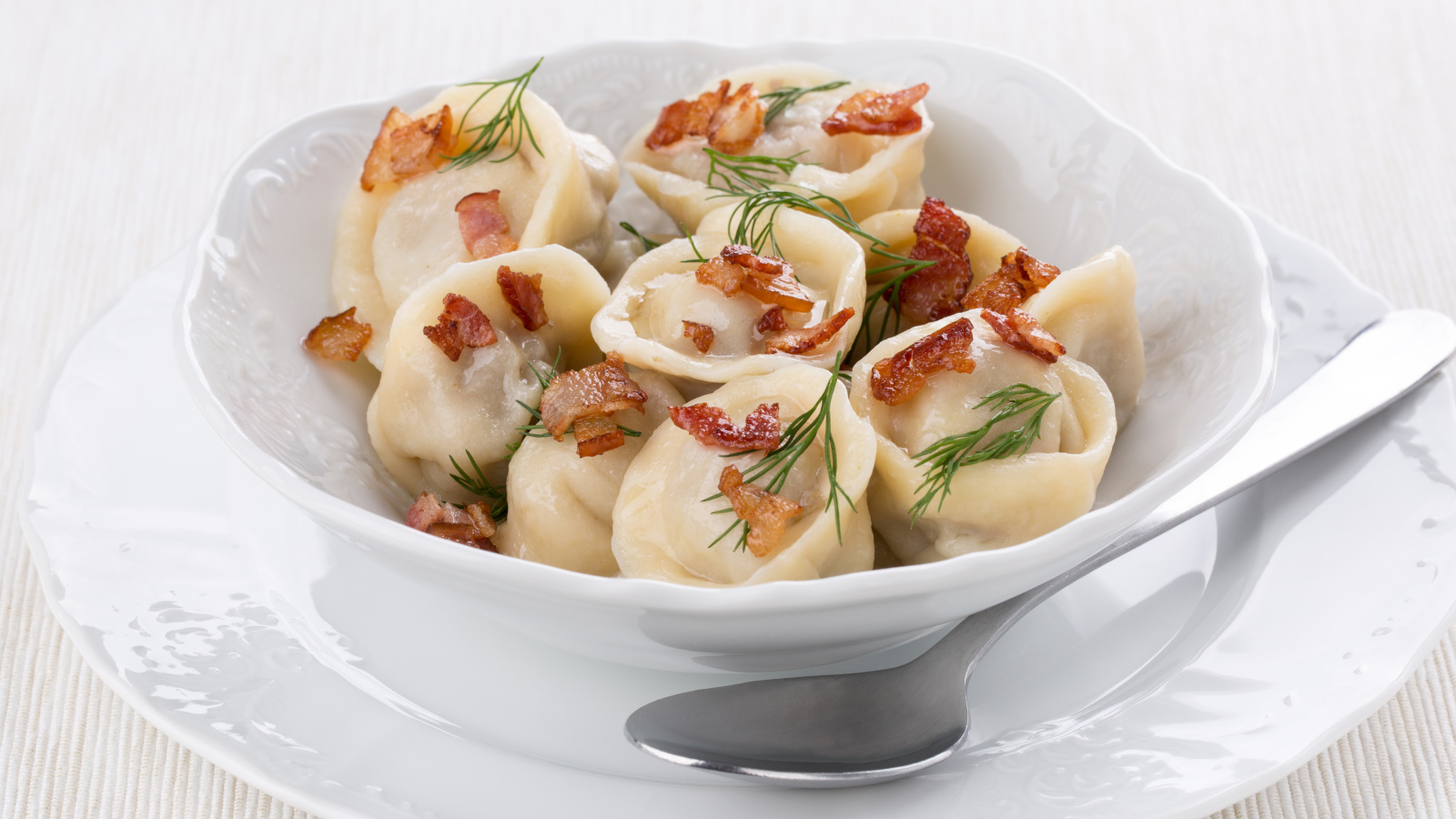 Аппетитные пельмени с салом и зеленью в белой тарелке