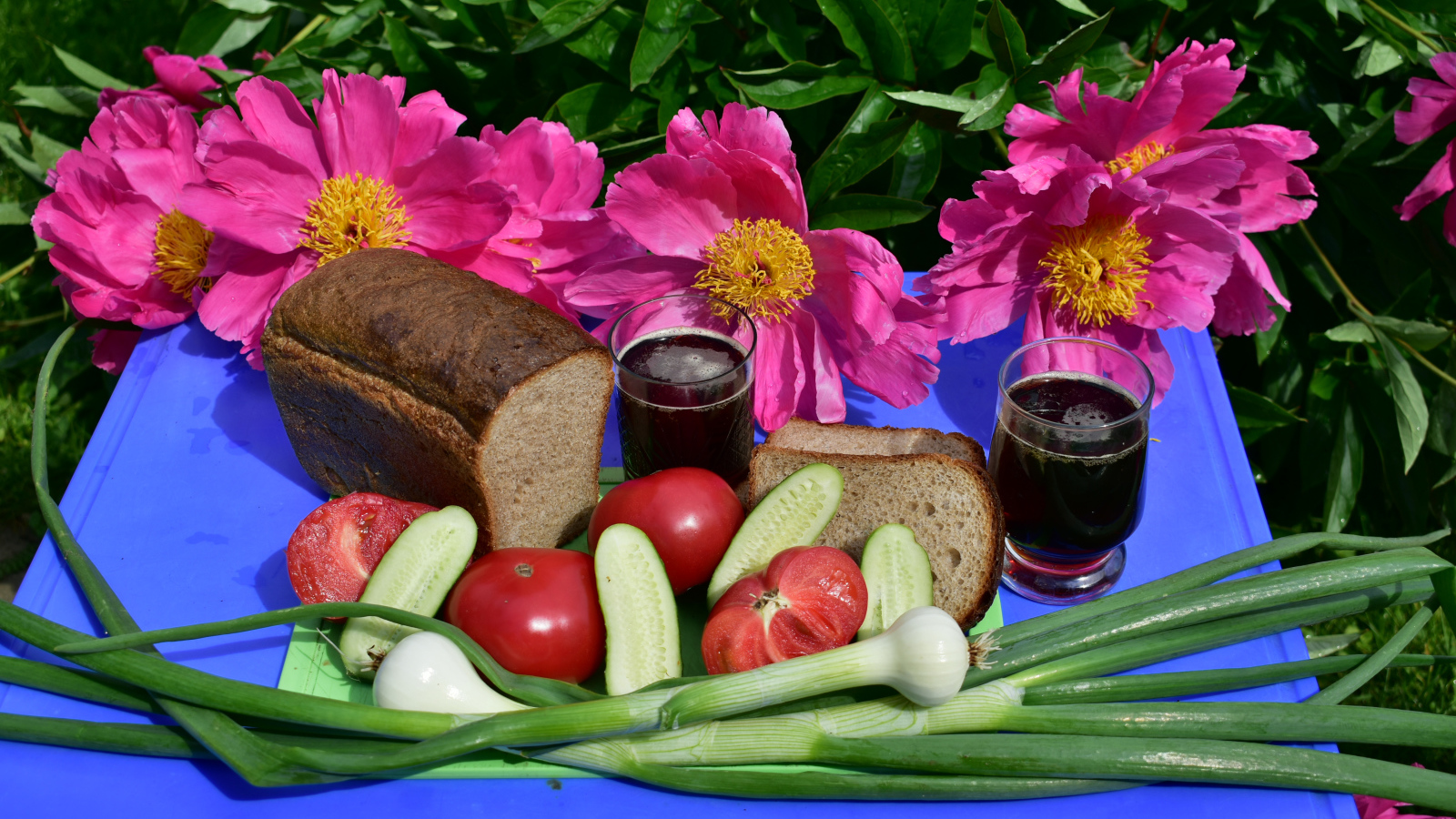 Черный хлеб, овощи и вино на фоне розовых пионов 