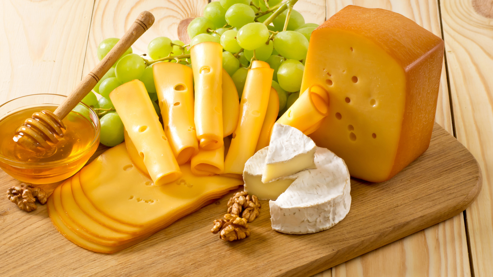 Cheese on the table with white grapes, honey and nuts