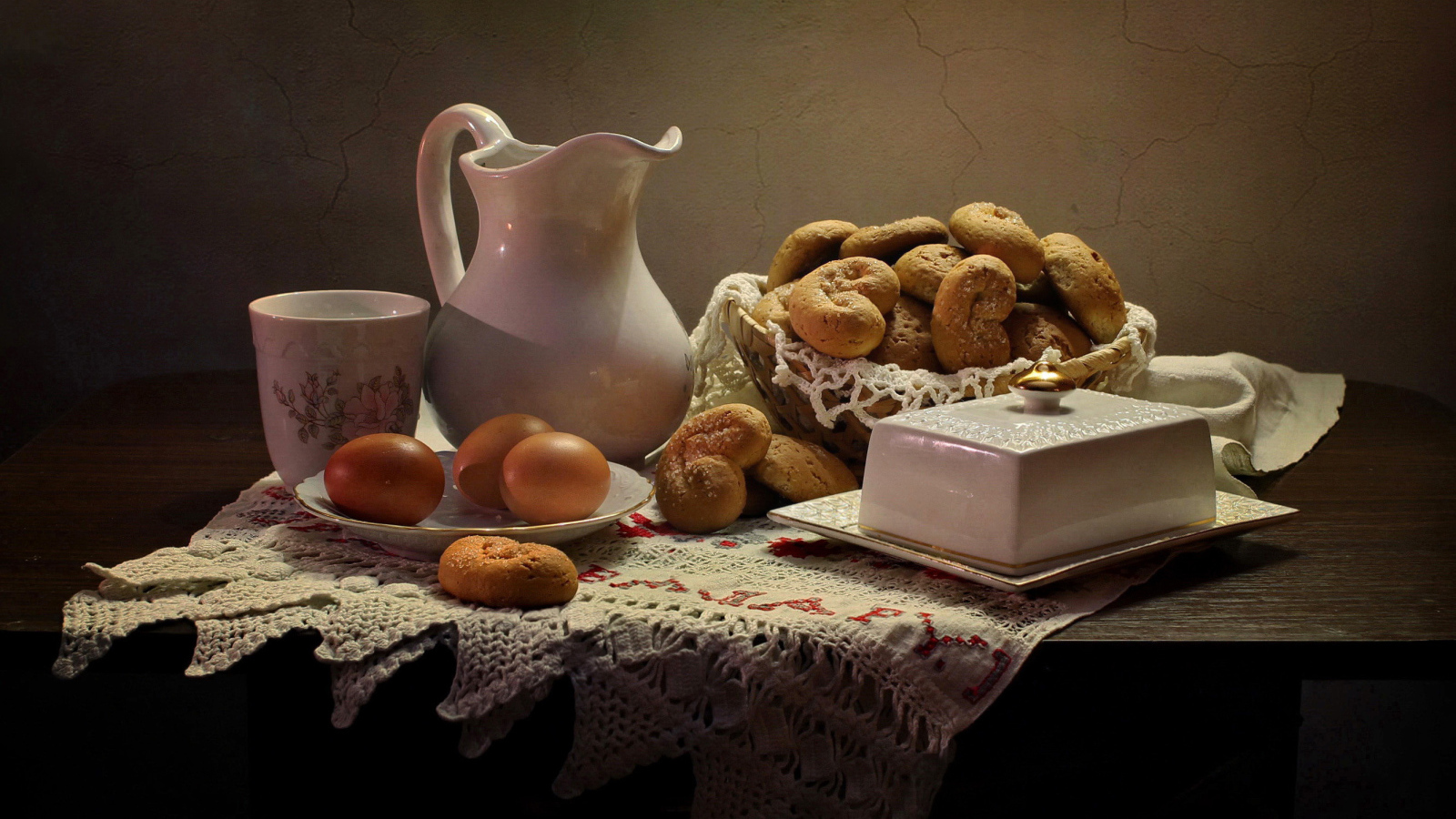 Вареные яйца на столе с кувшином, выпечкой и масленкой 