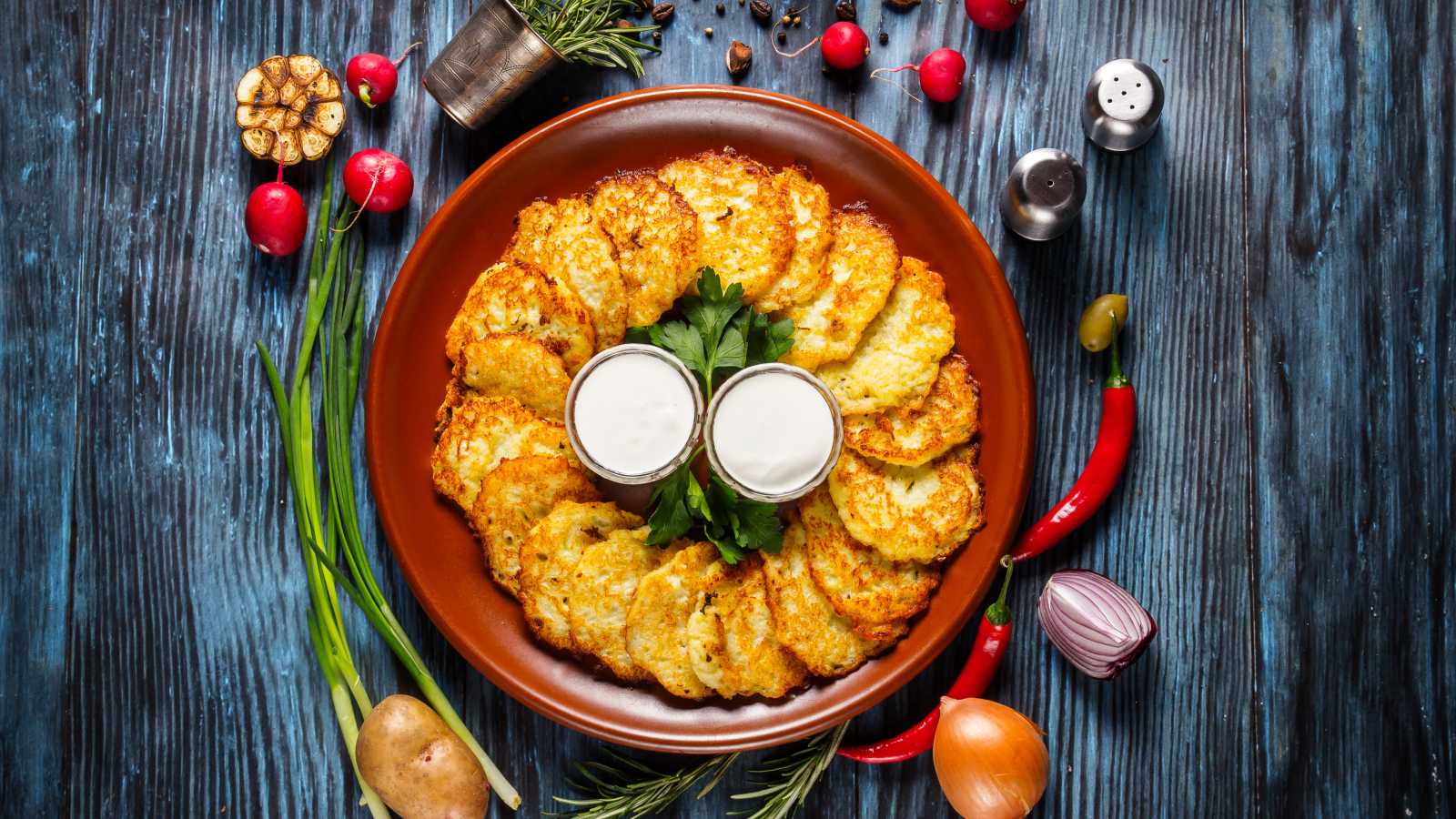 Драники с соусом на тарелке на столе с овощами