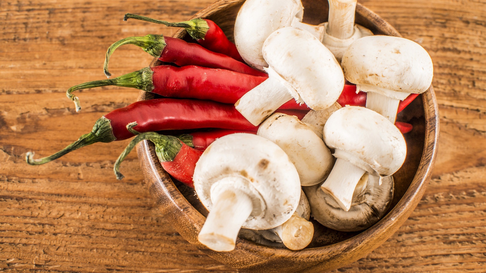 Грибы шампиньоны в деревянной миске с красным перцем