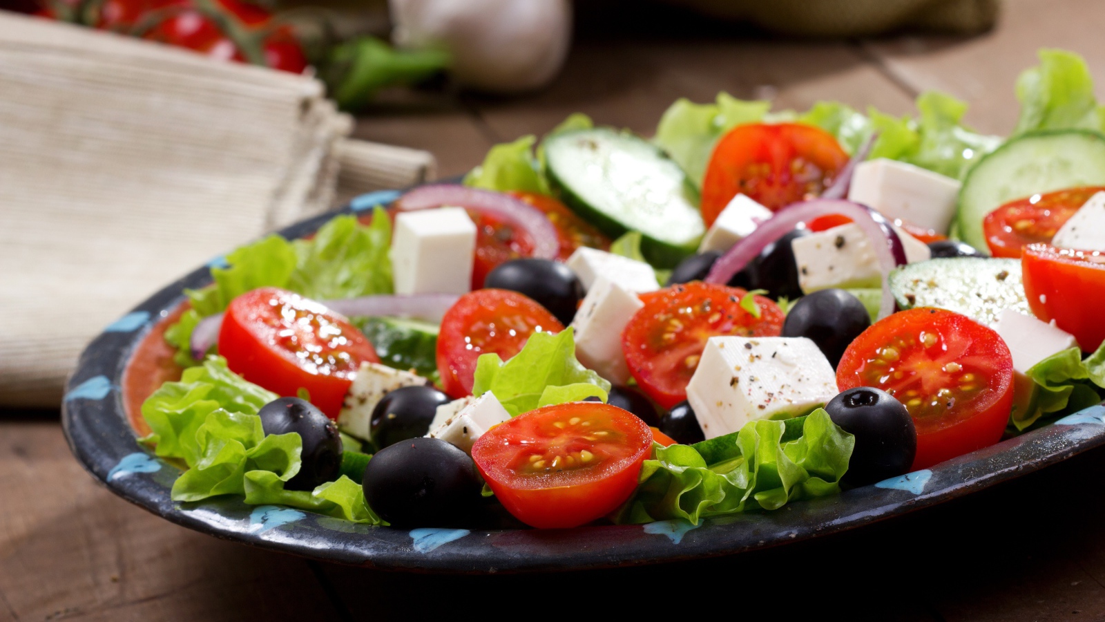 Салат с помидорами, огурцами, оливками, кусочками сыра и луком на листьях салата