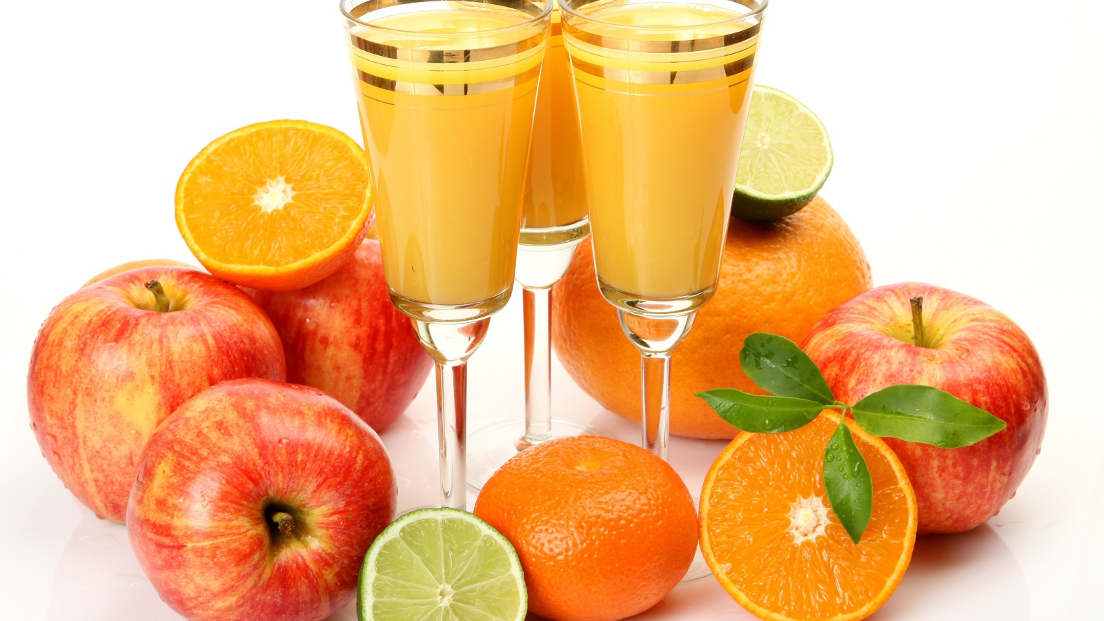 Три бокала сока на столе с яблоками и апельсинами на белом фоне