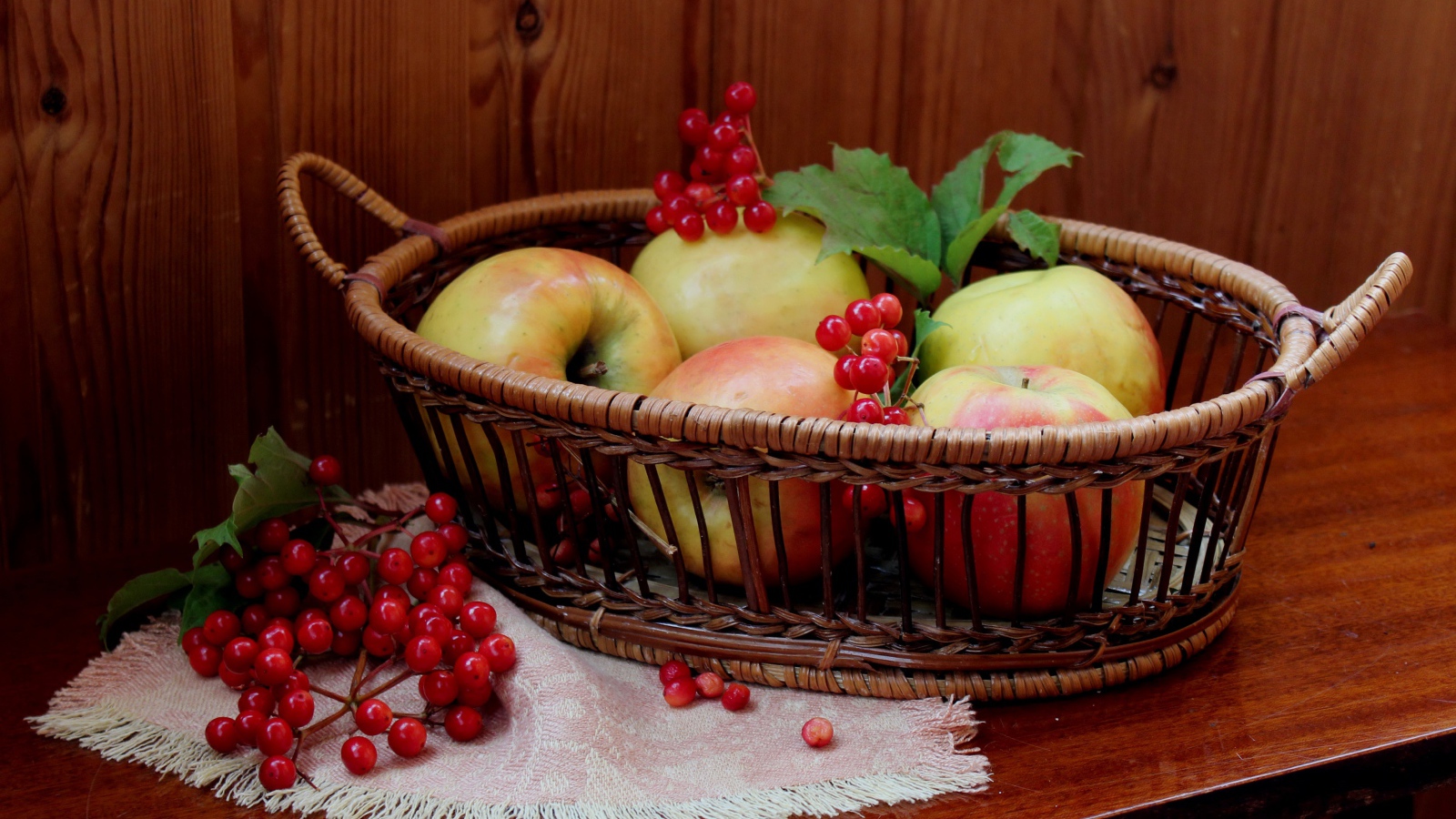 Красивые яблоки в корзине на столе с ягодами калины