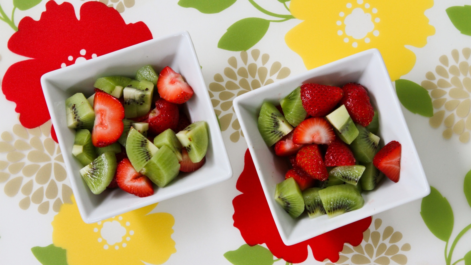 Салат с ягодами клубники и киви в белых тарелках на столе 