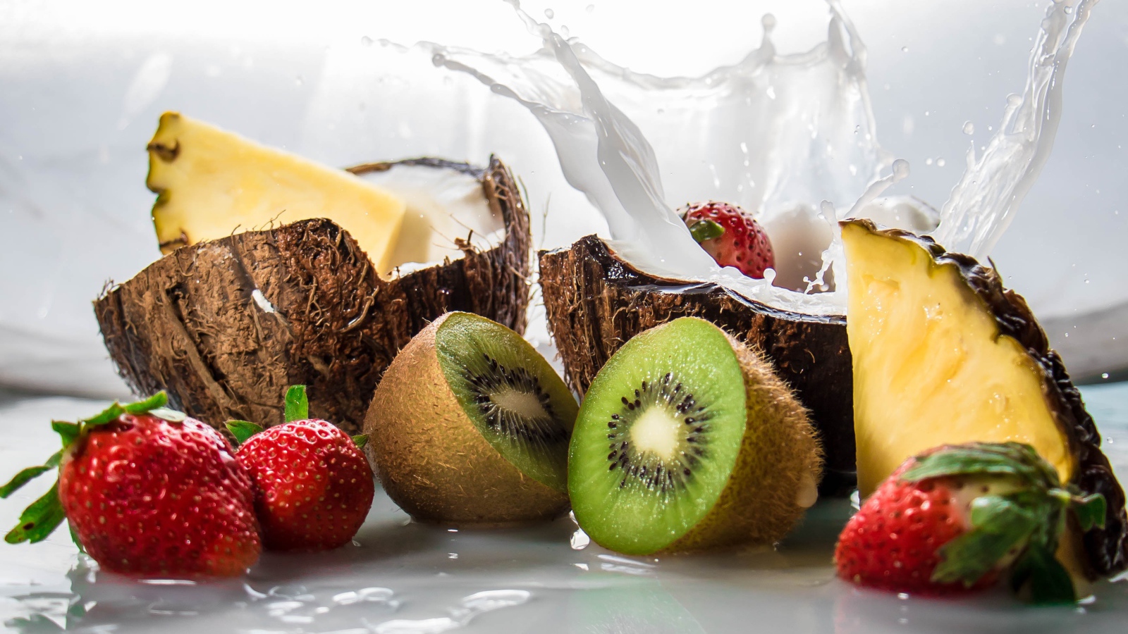 Тропические фрукты кокосы, ананасы и киви на белом фоне с клубникой