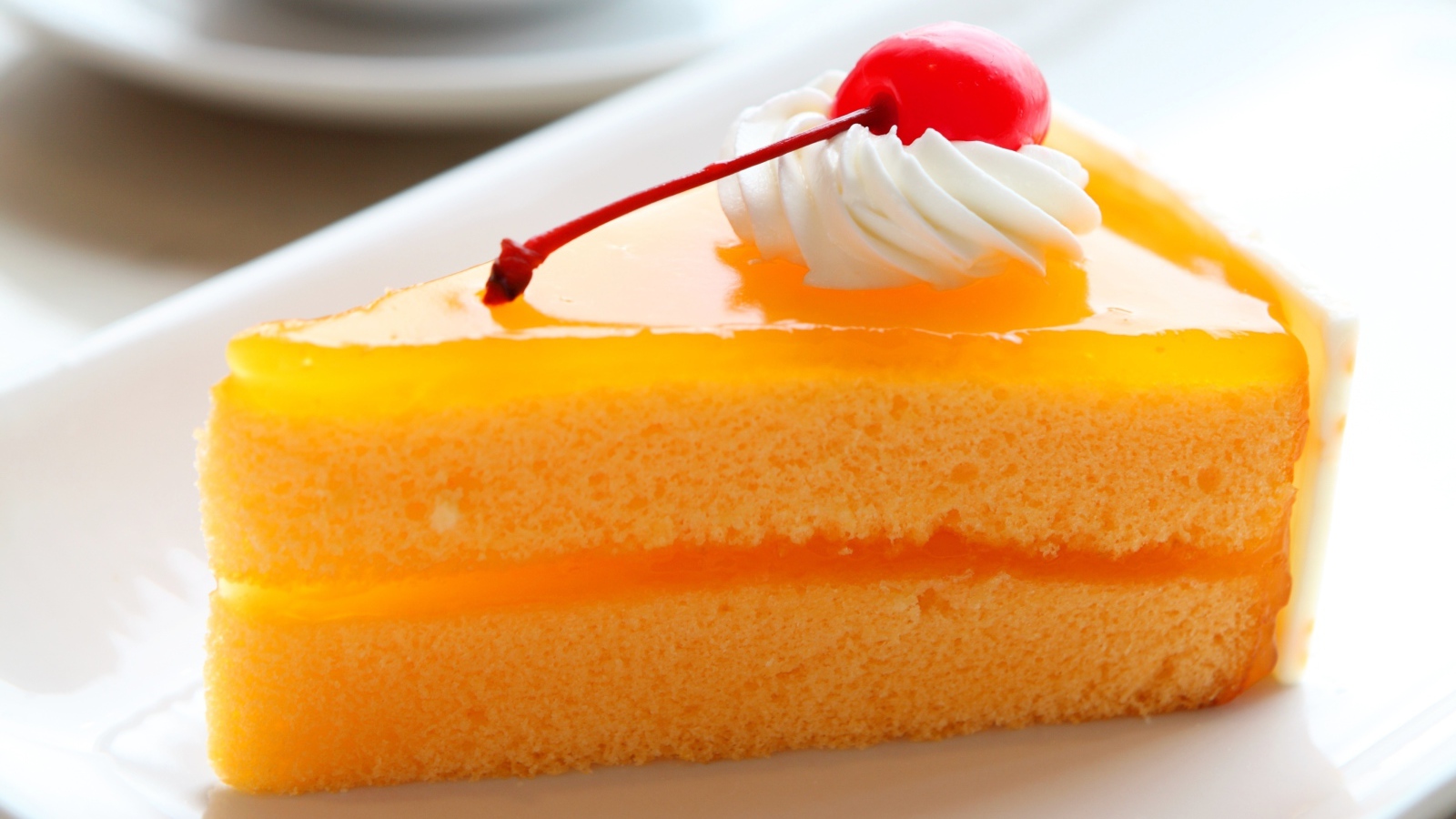 Кусок апельсинового торта с вишенкой на белой тарелке