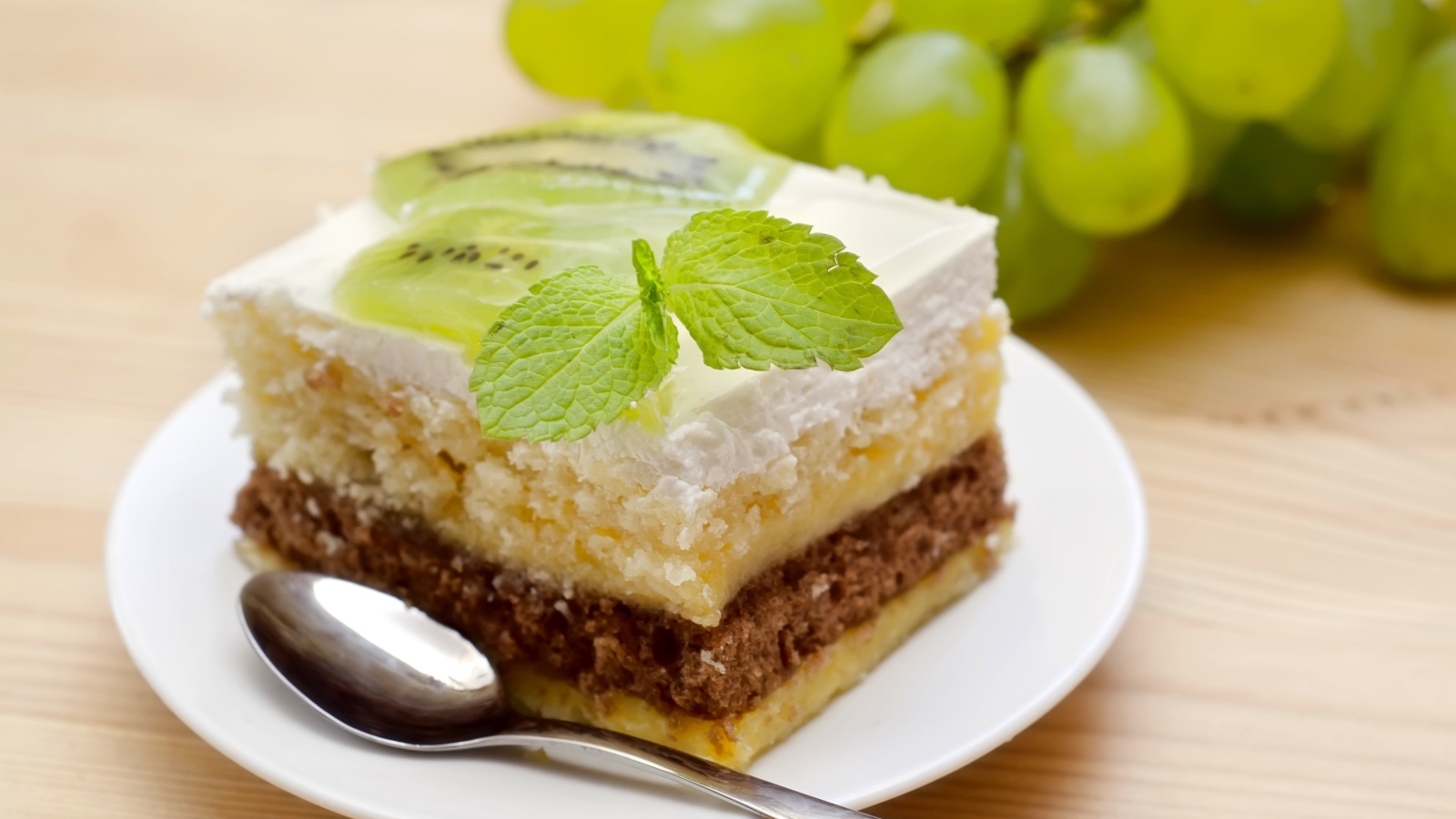 Кусок торта с киви и мятой на столе с виноградом