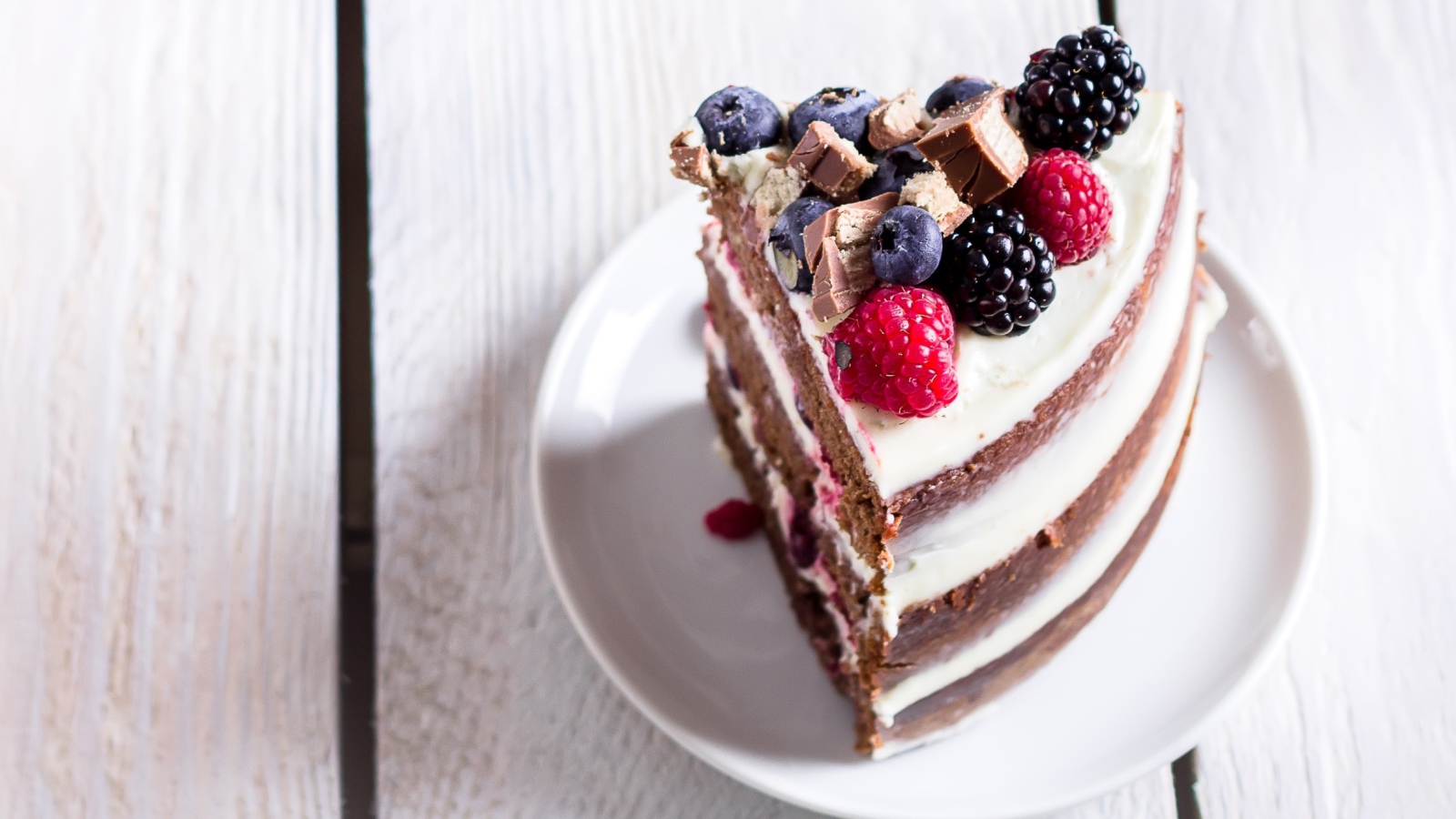 Кусок торта с ягодами малины и черники на блюдце