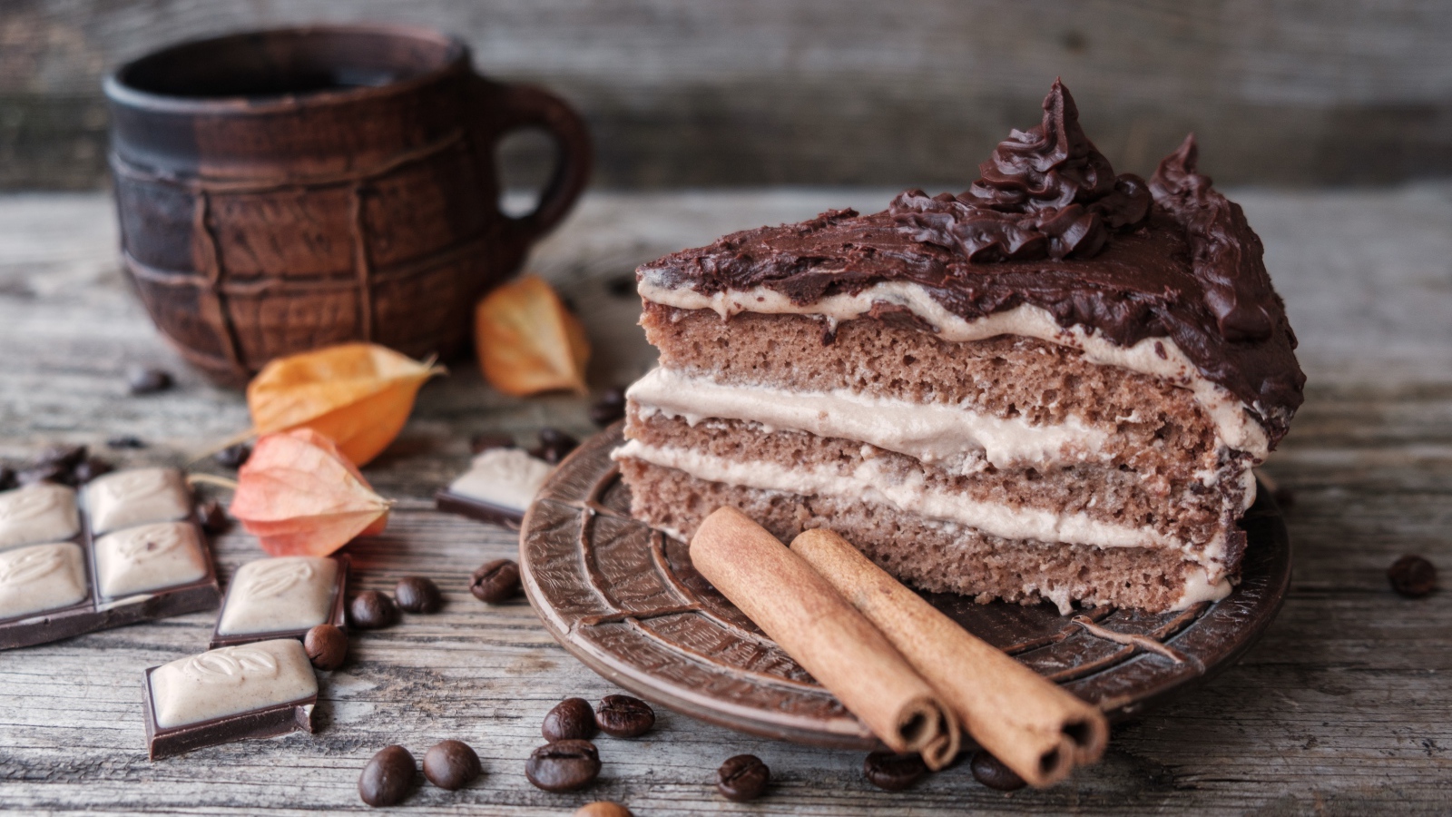 Кусок торта с корицей на столе с шоколадом и чашкой кофе