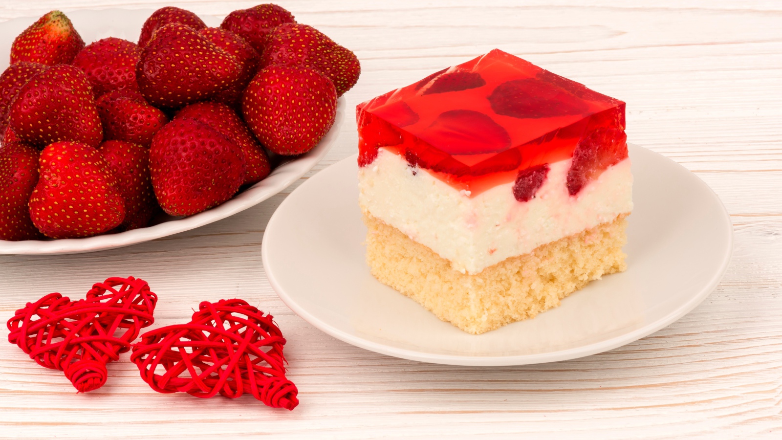 Пирожное на столе с клубникой и красными плетеными сердечками