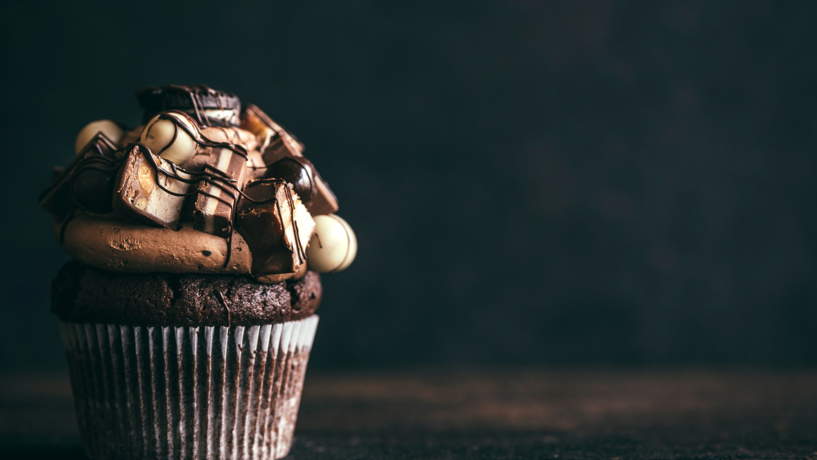 Шоколадный кекс с кремом и конфетами на сером фоне