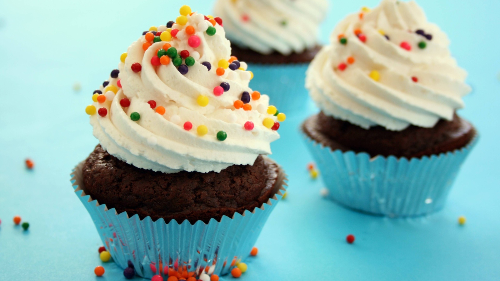 Шоколадные кексы со сливками и цветными брызгами на голубом фоне