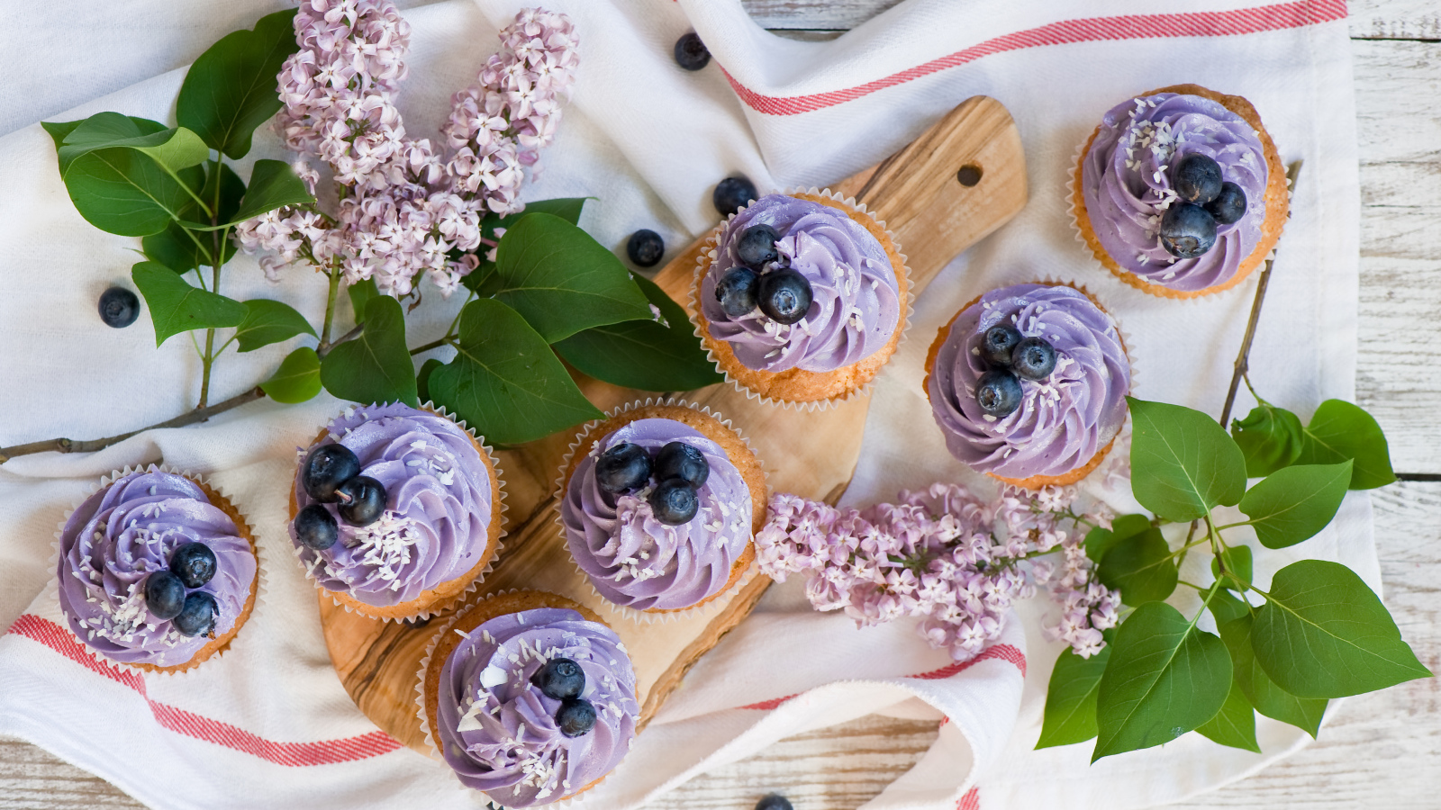 Кексы с кремом и ягодами черники на столе с ветками сирени 
