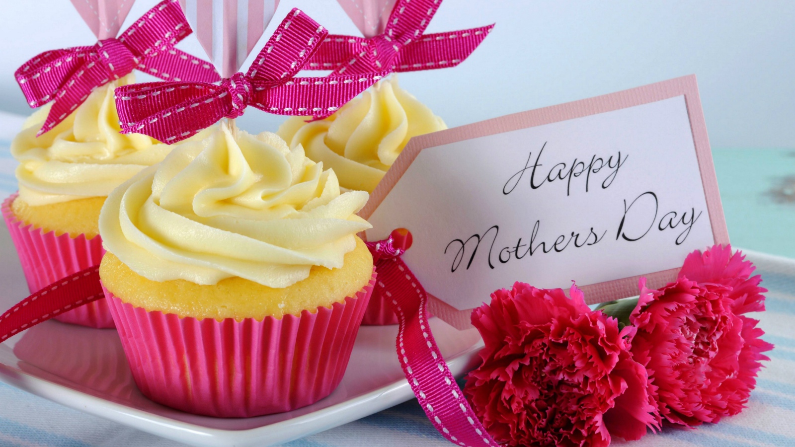 Кексы с кремом рядом с гвоздиками и пожеланиями к Дню матери