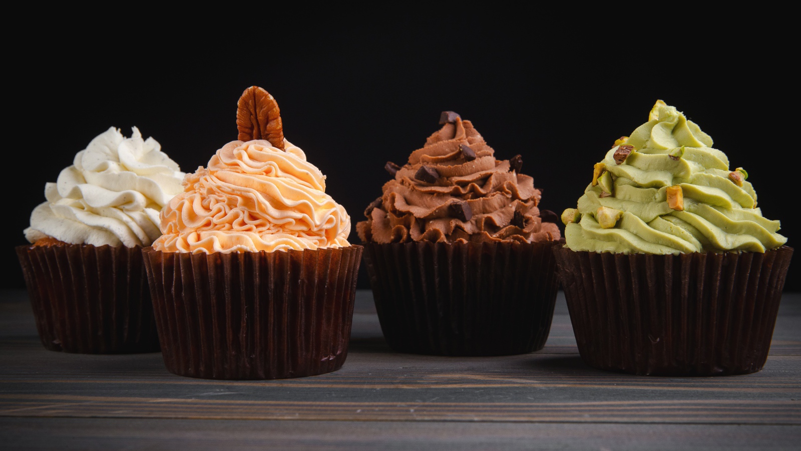 Четыре аппетитных капкейка с кремом на черном фоне