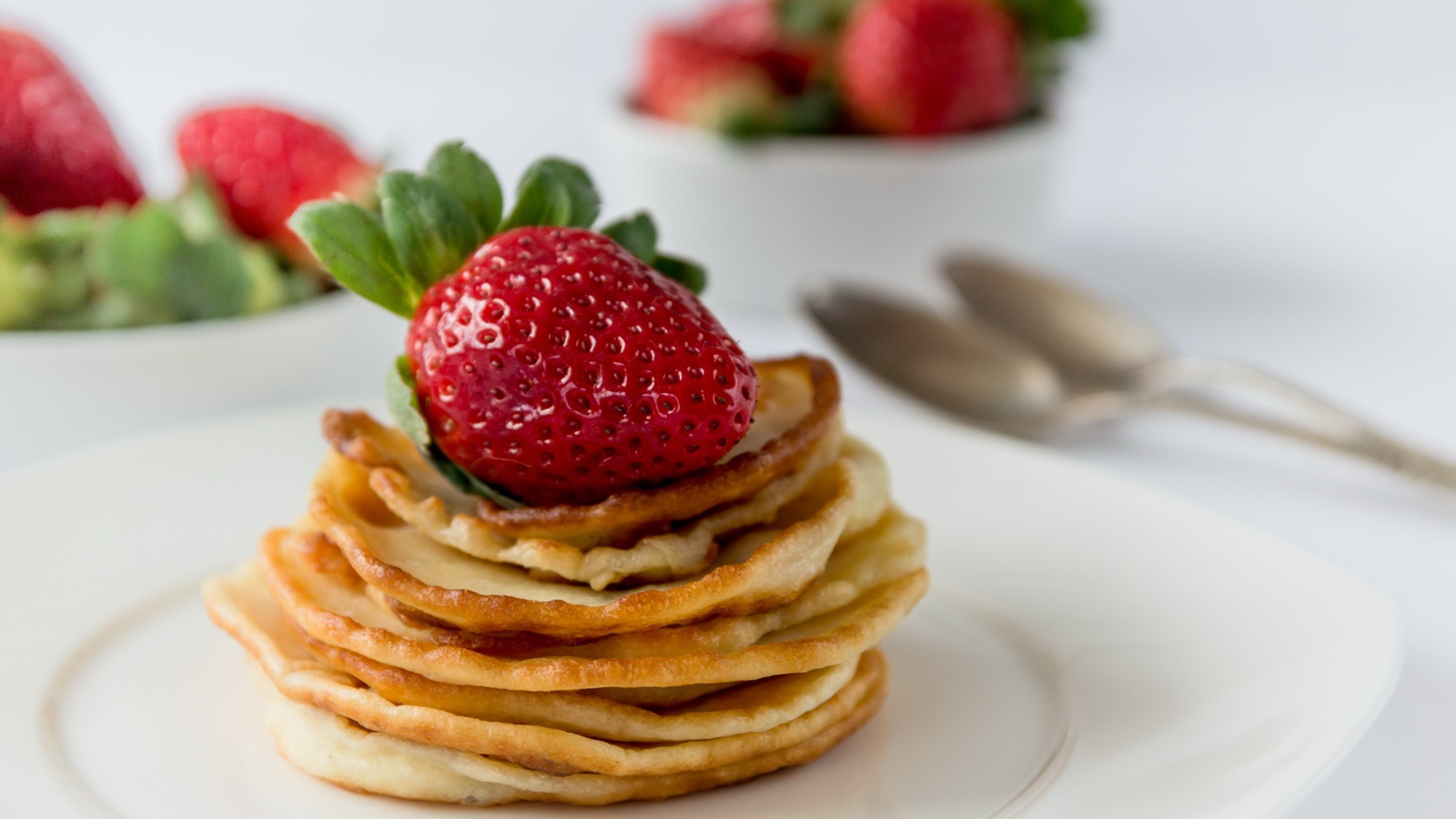 Оладьи с ягодами свежей клубники на белой тарелке 