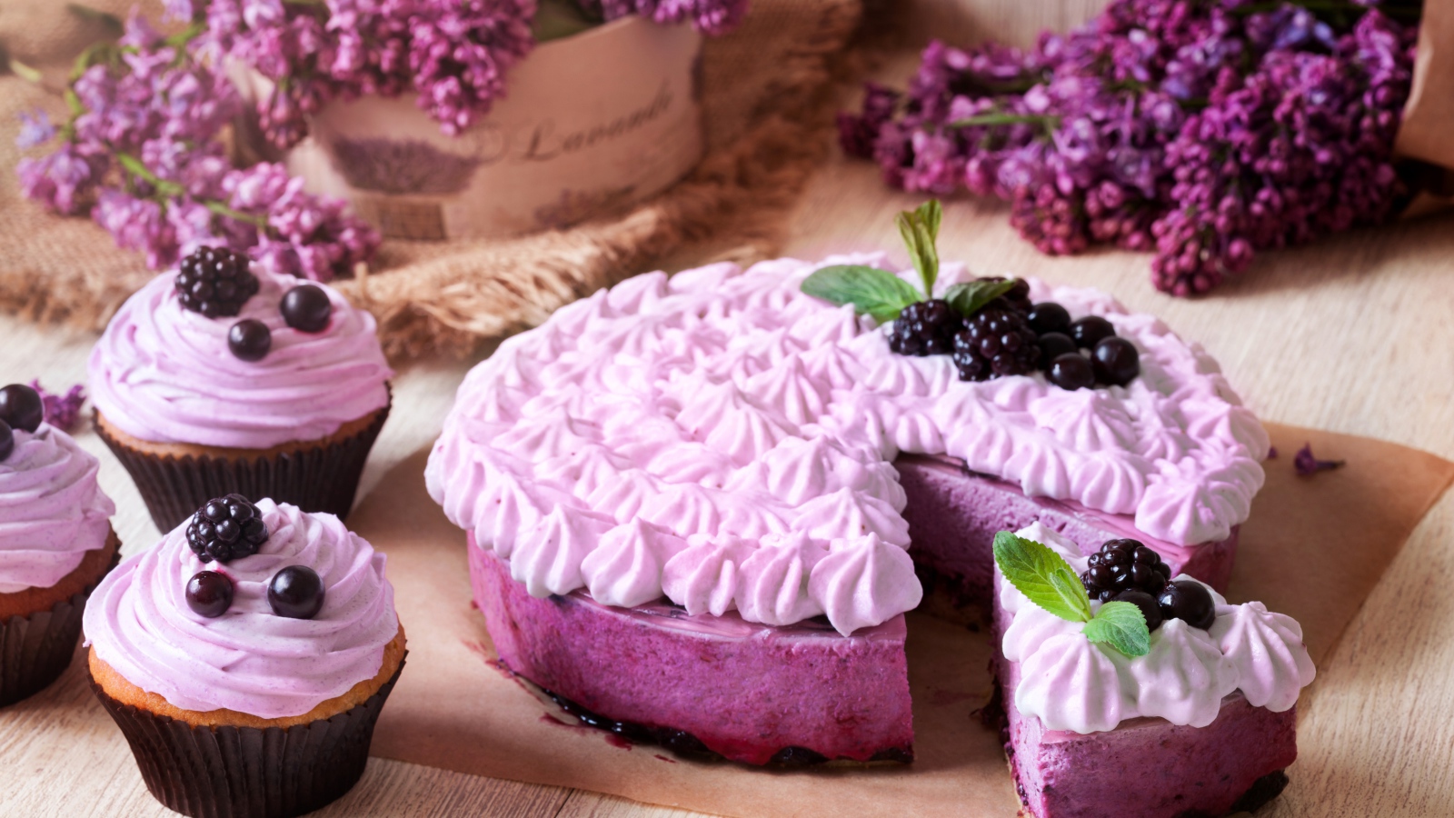 Пирог с кремом и вкусными кексами с черникой на столе с цветами сирени