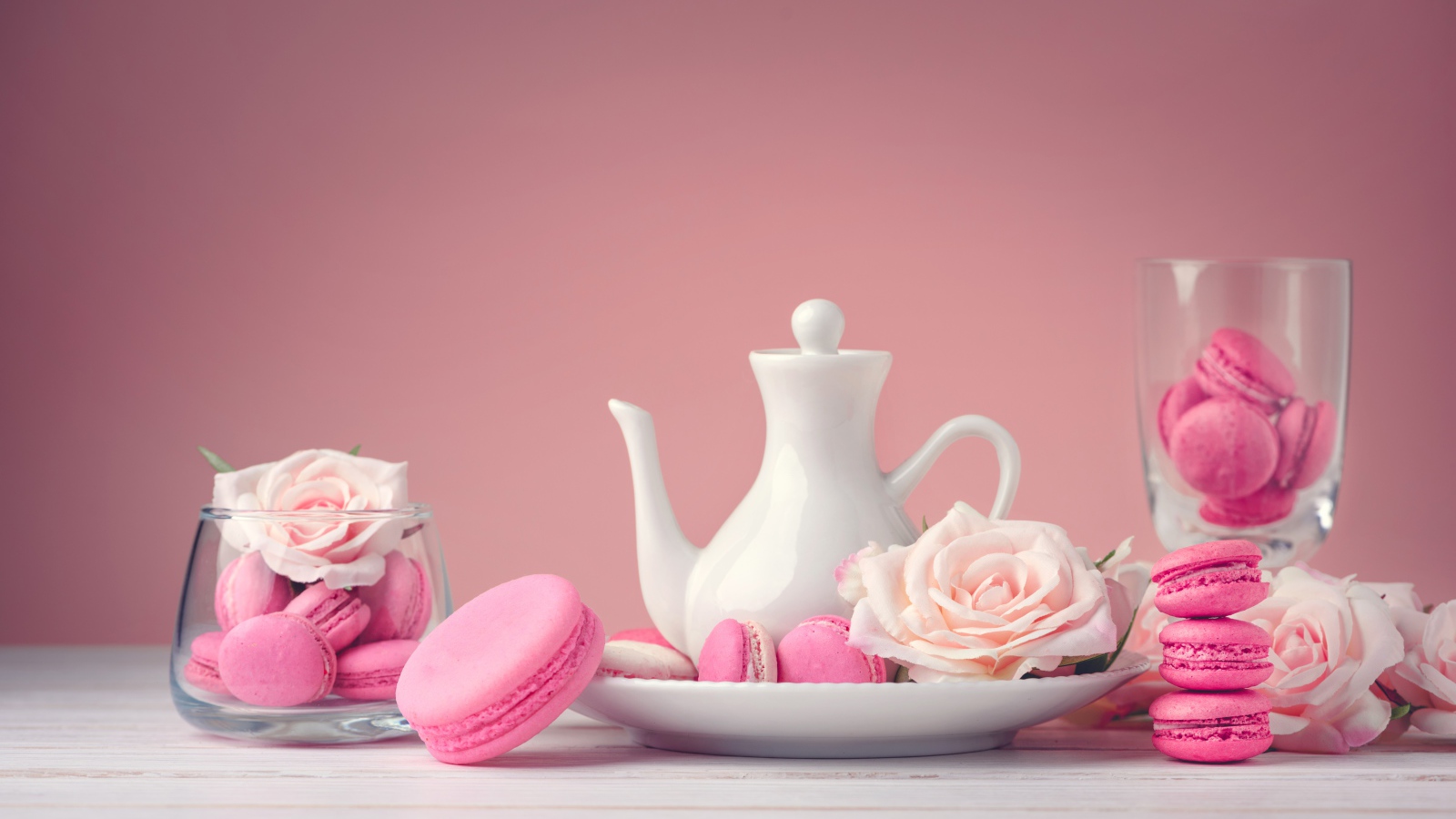 Розовый десерт макарун на столе с белый чайником и цветами розы