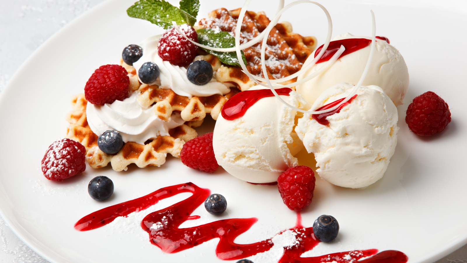 Сладкие вафли с ягодами черники и малины на белой тарелки с шариками мороженого