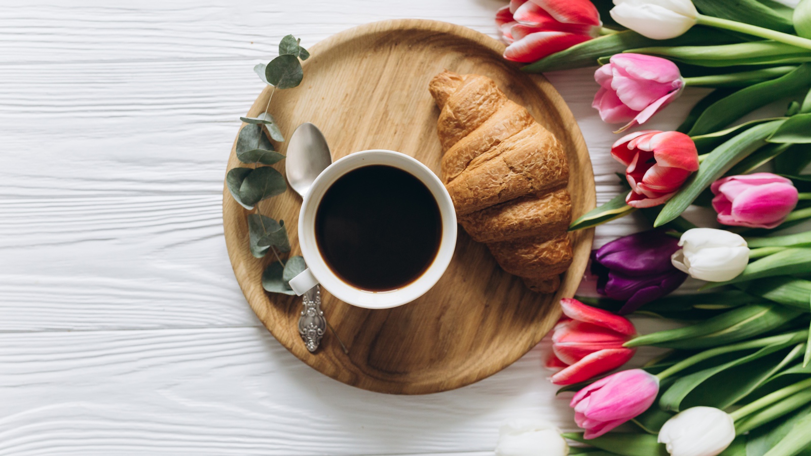 Чашка кофе с круассаном на столе с букетом тюльпанов 