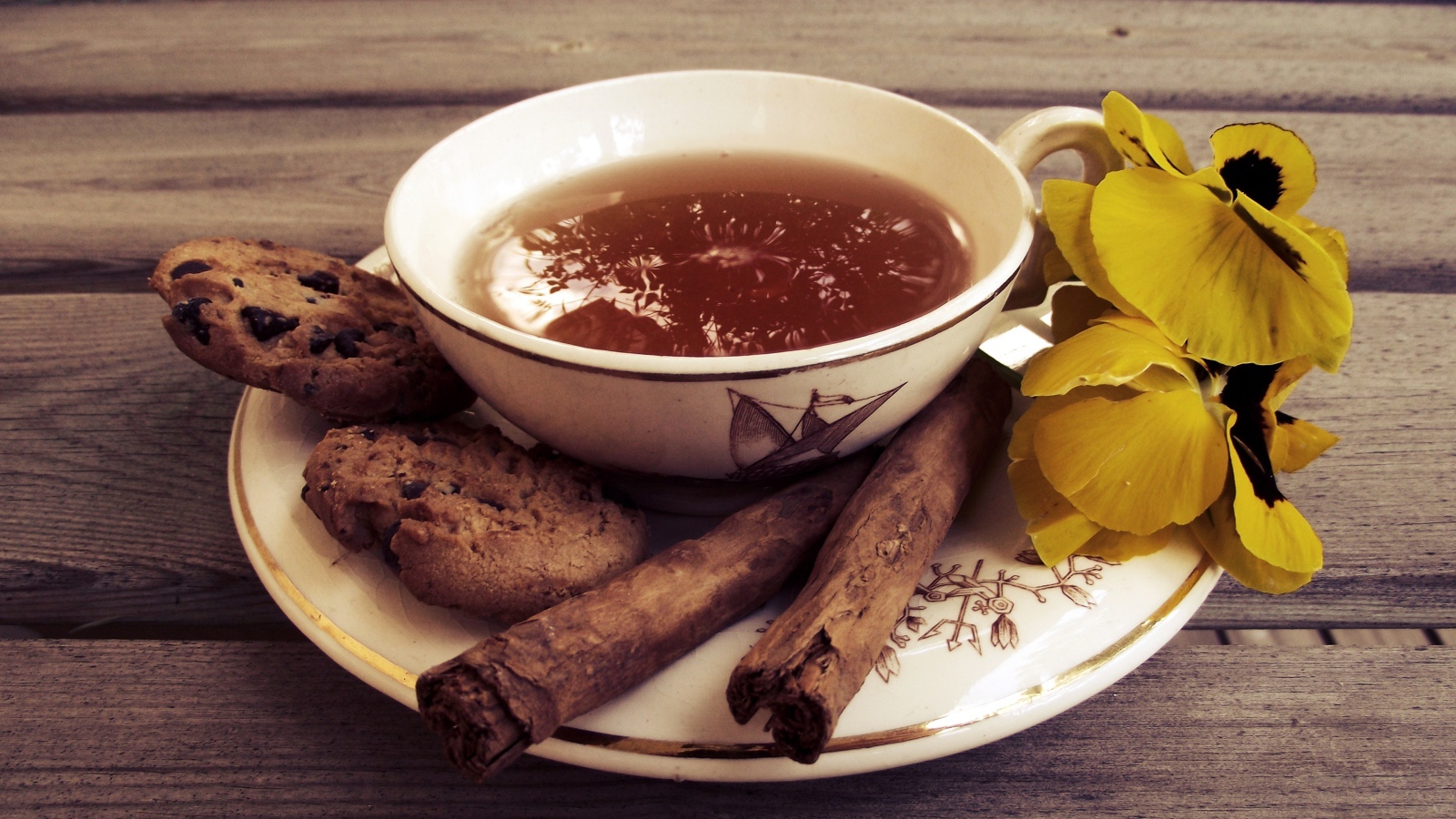 Чашка чая с печеньем, палочками корицы и цветами 