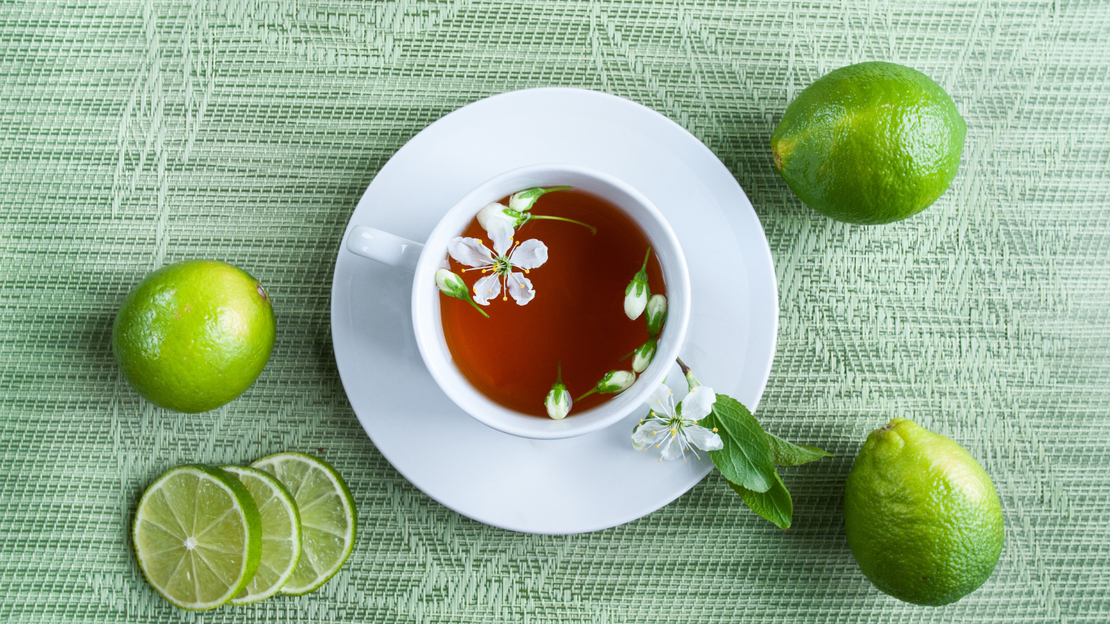 Чашка чая с зелеными лаймами на столе