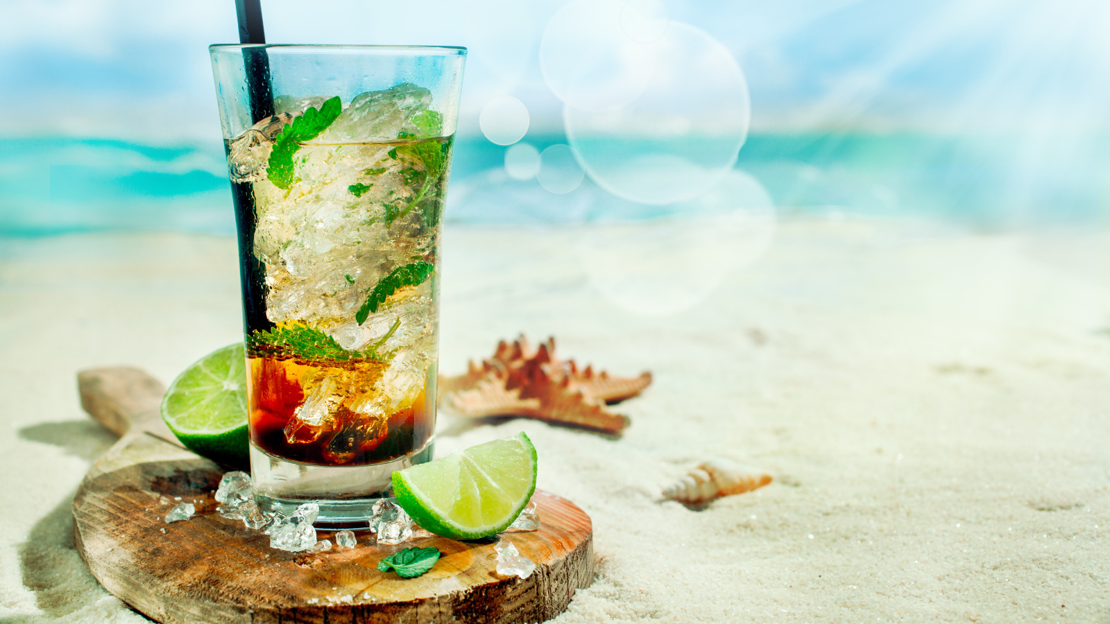 Коктейль в стакане с лаймом и кубиками льда стоит на песке на пляже