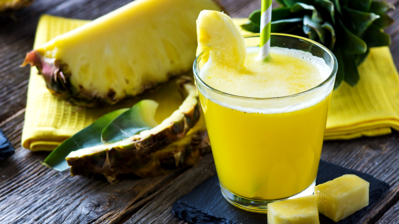 Ананасовый напиток в стакане на столе со свежими ананасами