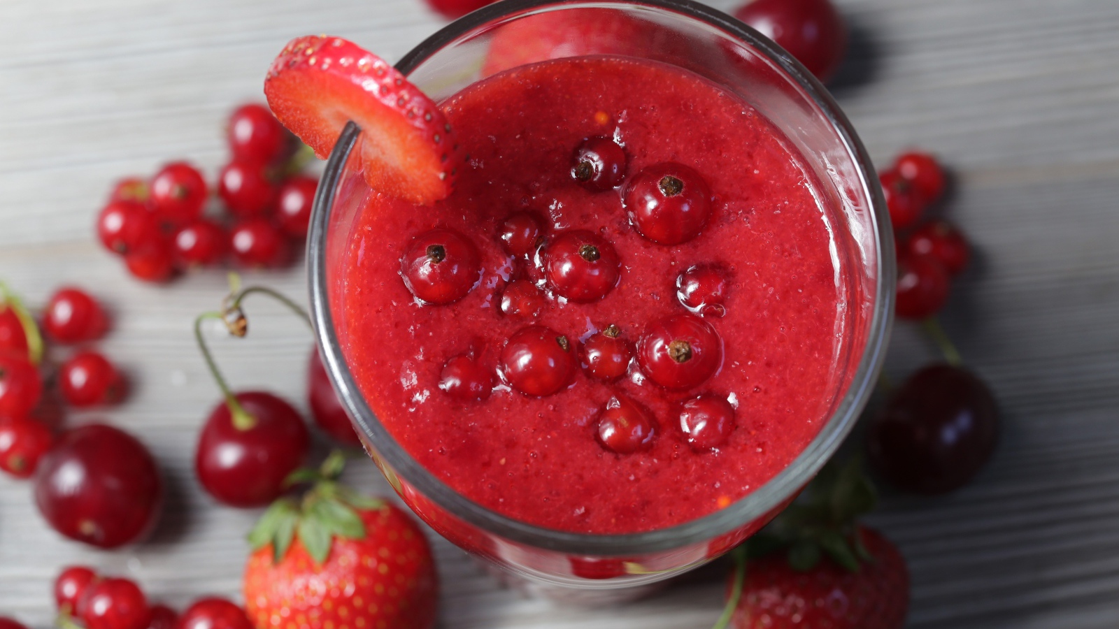 Смузи в стакане с ягодами клубники, красной смородины и вишни