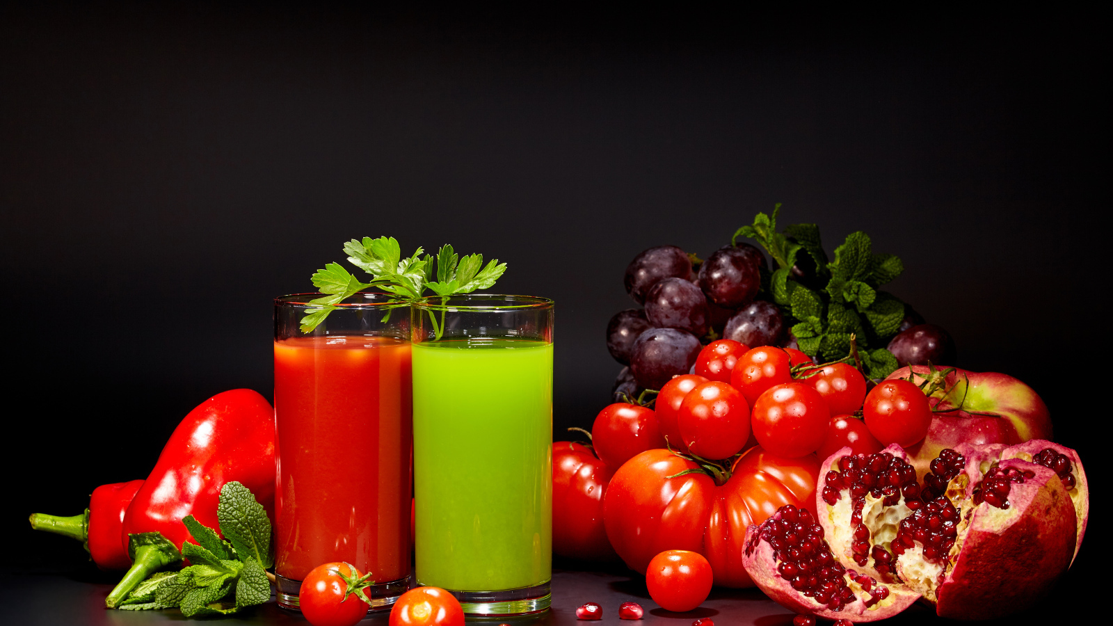 Два стакана сока на столе со свежими помидорами, перцем, гранатом, виноградом и зеленью
