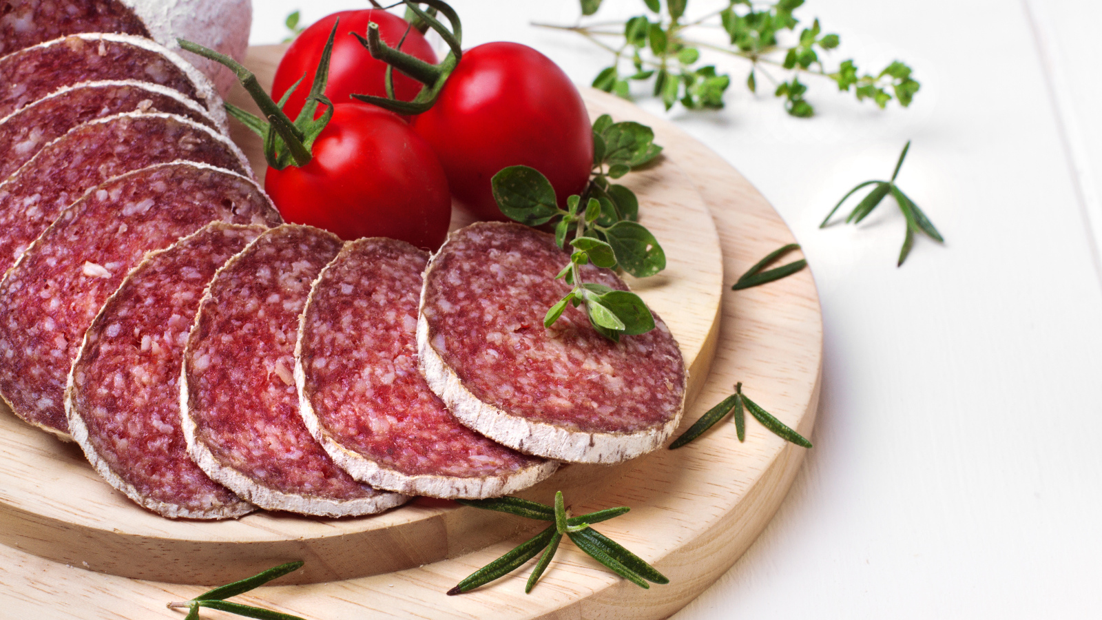 Вкусная колбаса на разделочной доске с помидорами и зеленью 