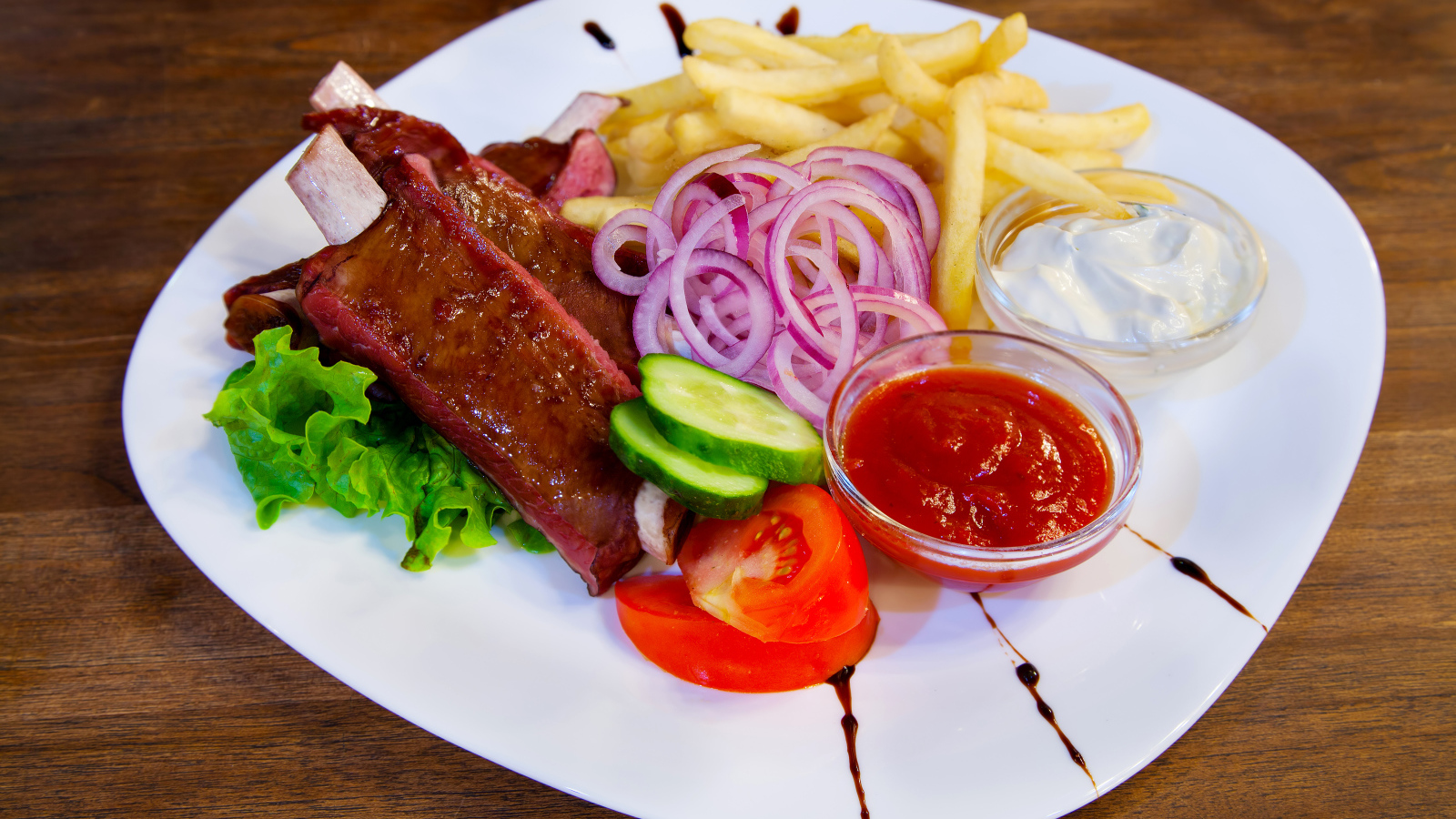 Мясо с овощами и картофелем фри на большой белой тарелке с соусом