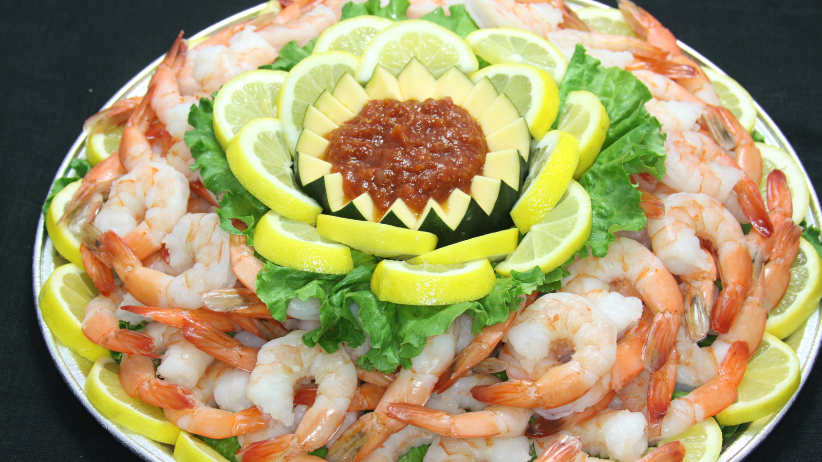 Вареные креветки с лимоном и соусом на большой тарелке