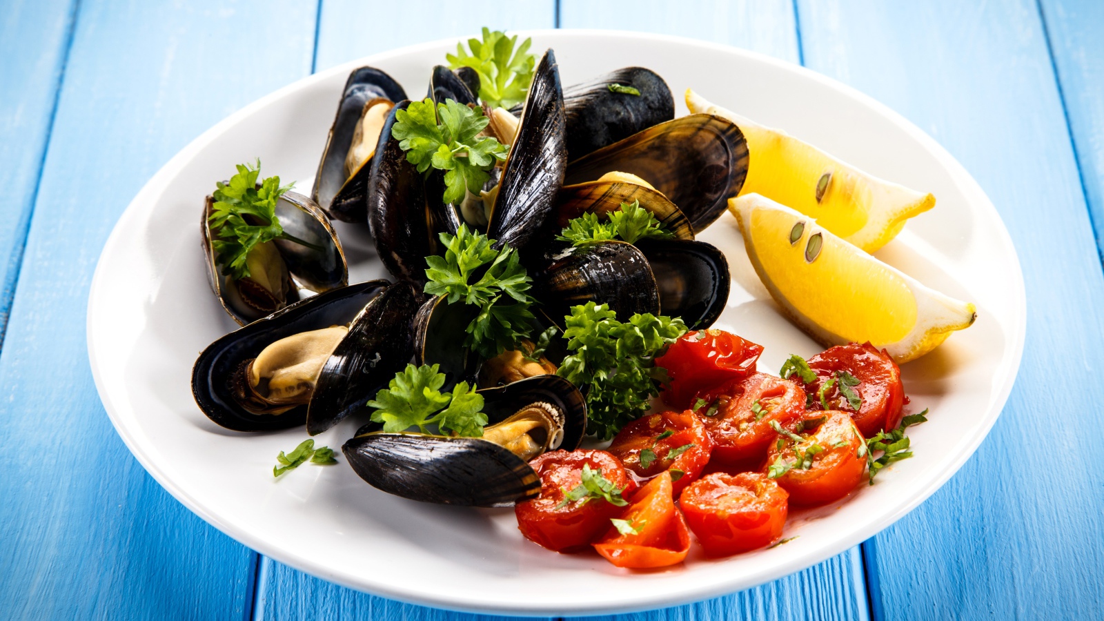 Мидии с томатами, кусочками лимона и зеленью петрушки на белой тарелке