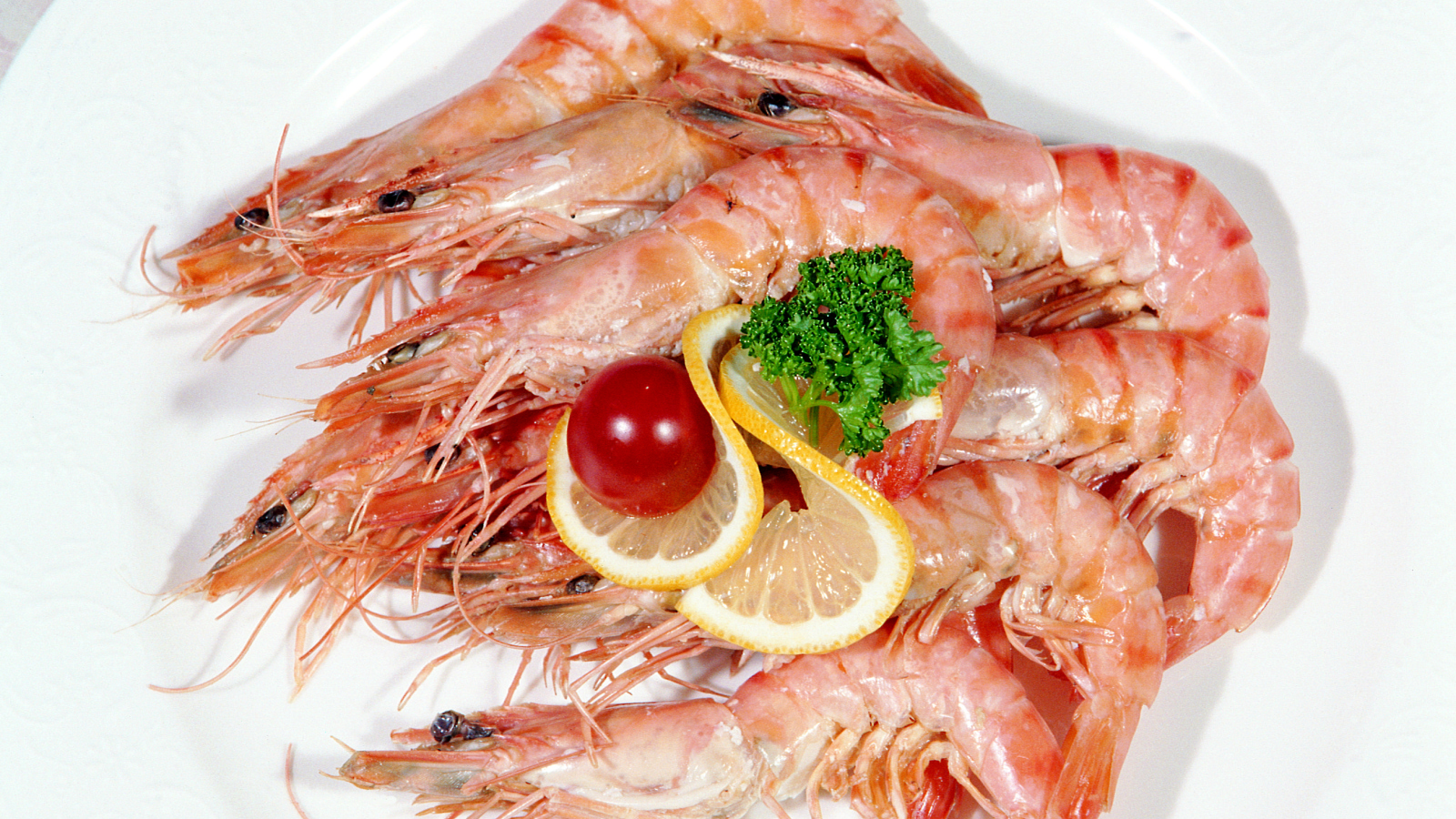 Креветки с лимоном и помидором на белой тарелке