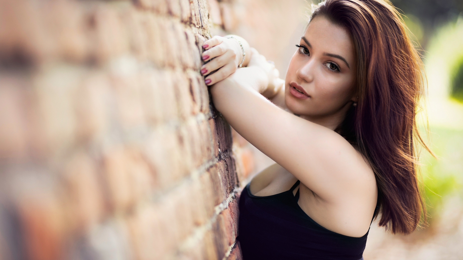 Нежная  девушка шатенка стоит у кирпичной стены