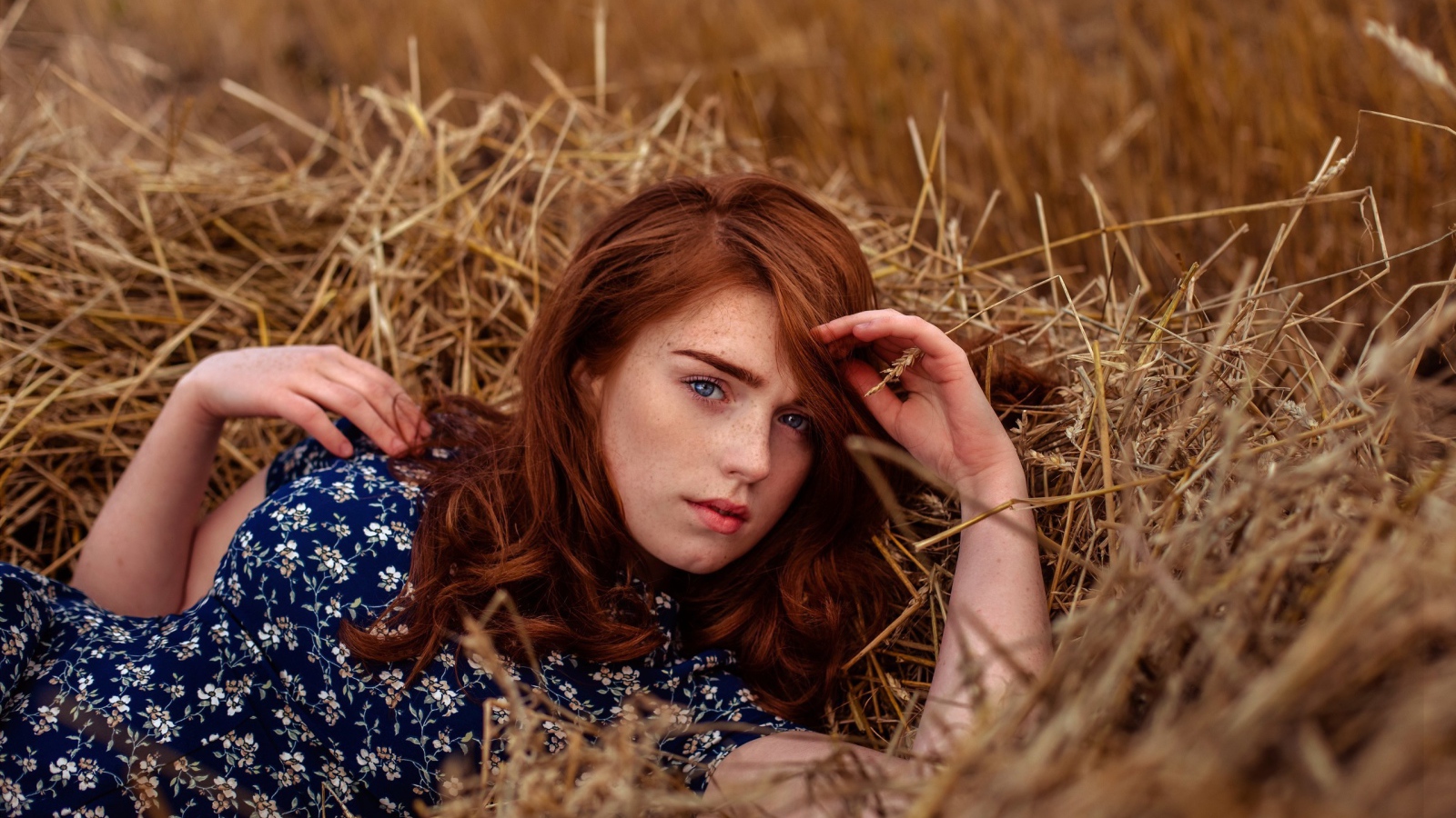 Красивая голубоглазая рыжеволосая девушка лежит в сене