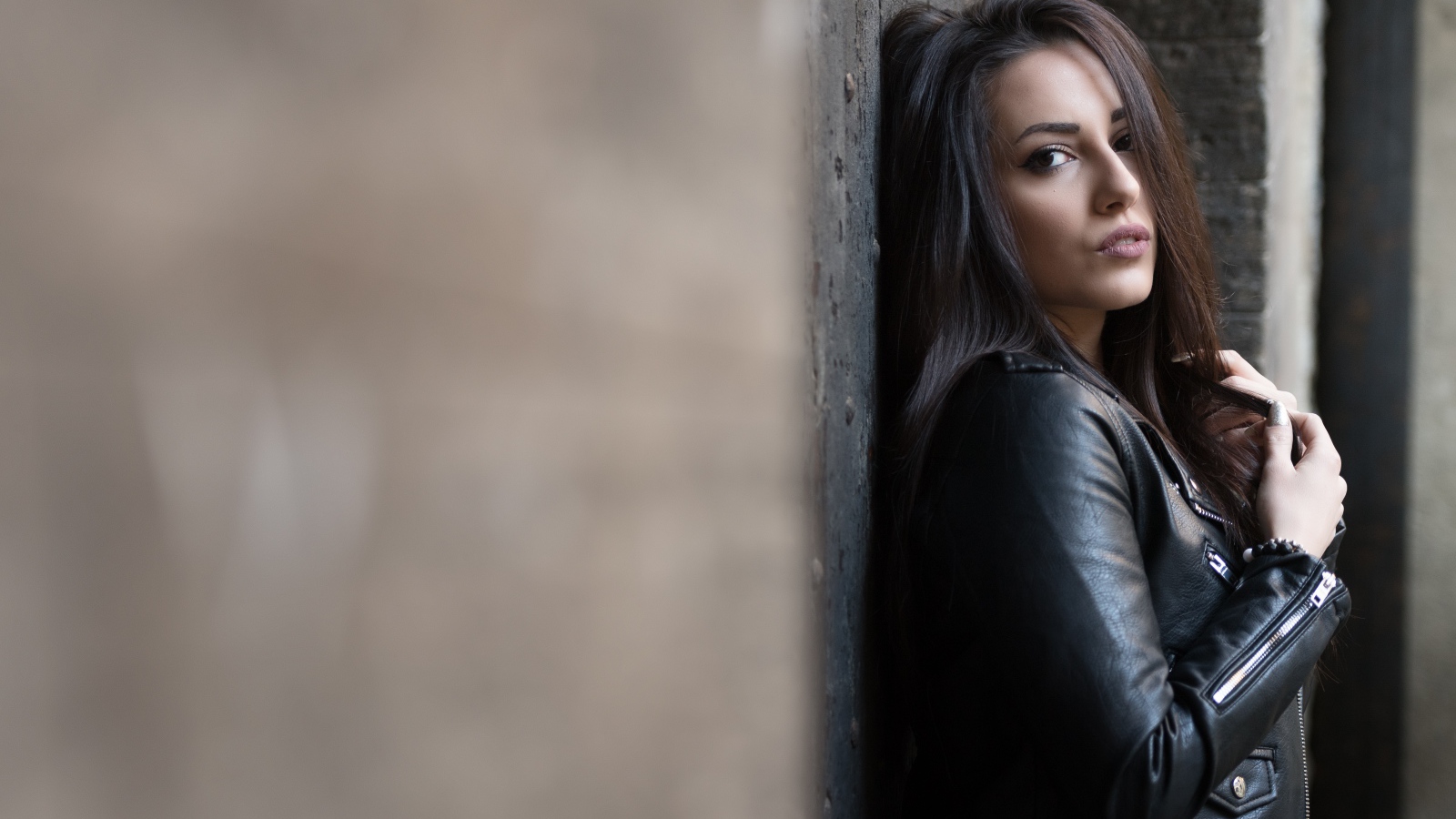 Красивая  брюнетка в кожаной куртке стоит у стены