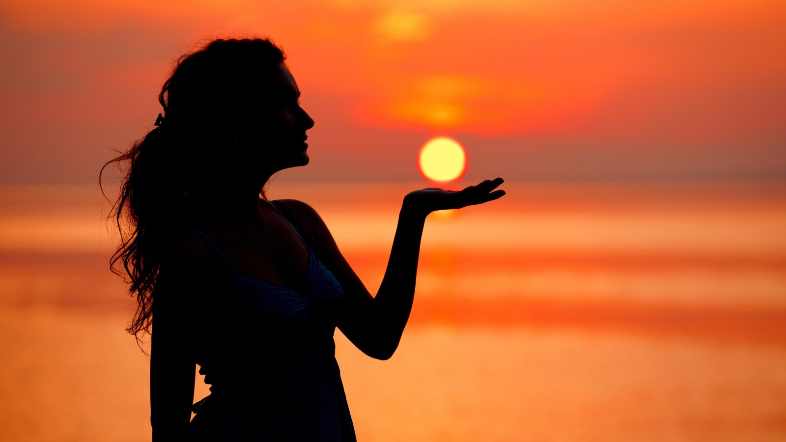 Красивая девушка держит солнце в ладони на закате