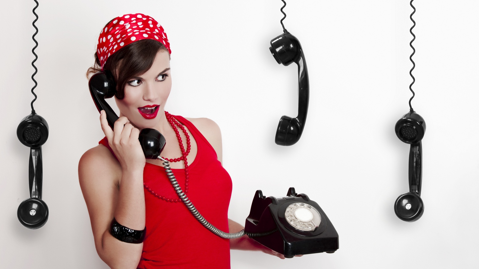 Красивая девушка в красном с черным старым телефоном в руках