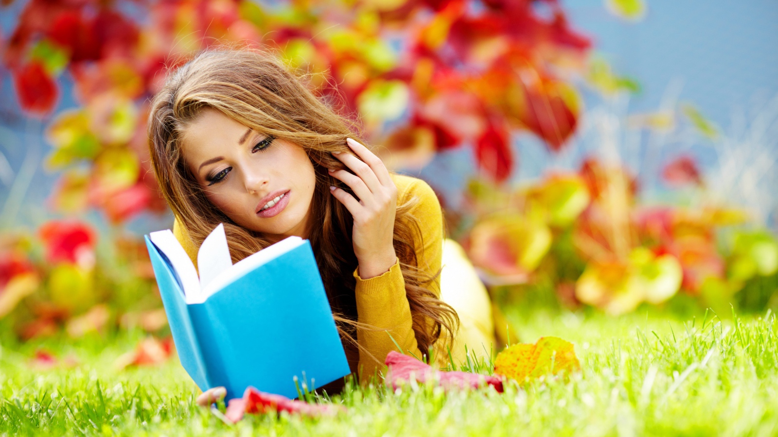 Красивая девушка читает книгу лежа на зеленой траве