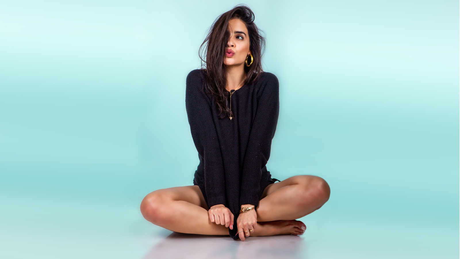 Красивая девушка сидит в черном свитере на голубом фоне
