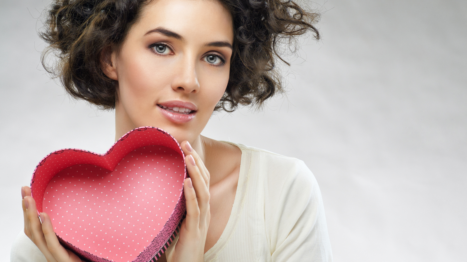 Красивая девушка с коробкой в форме сердца в руках на сером фоне