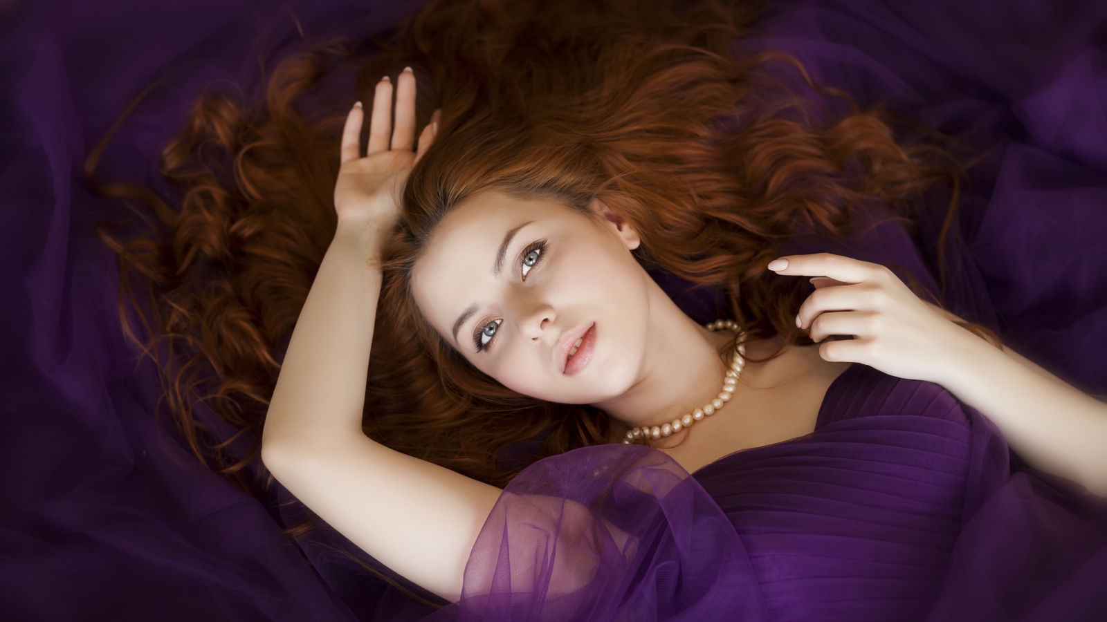 Красивая рыжеволосая девушка в лежит в фиолетовом платье