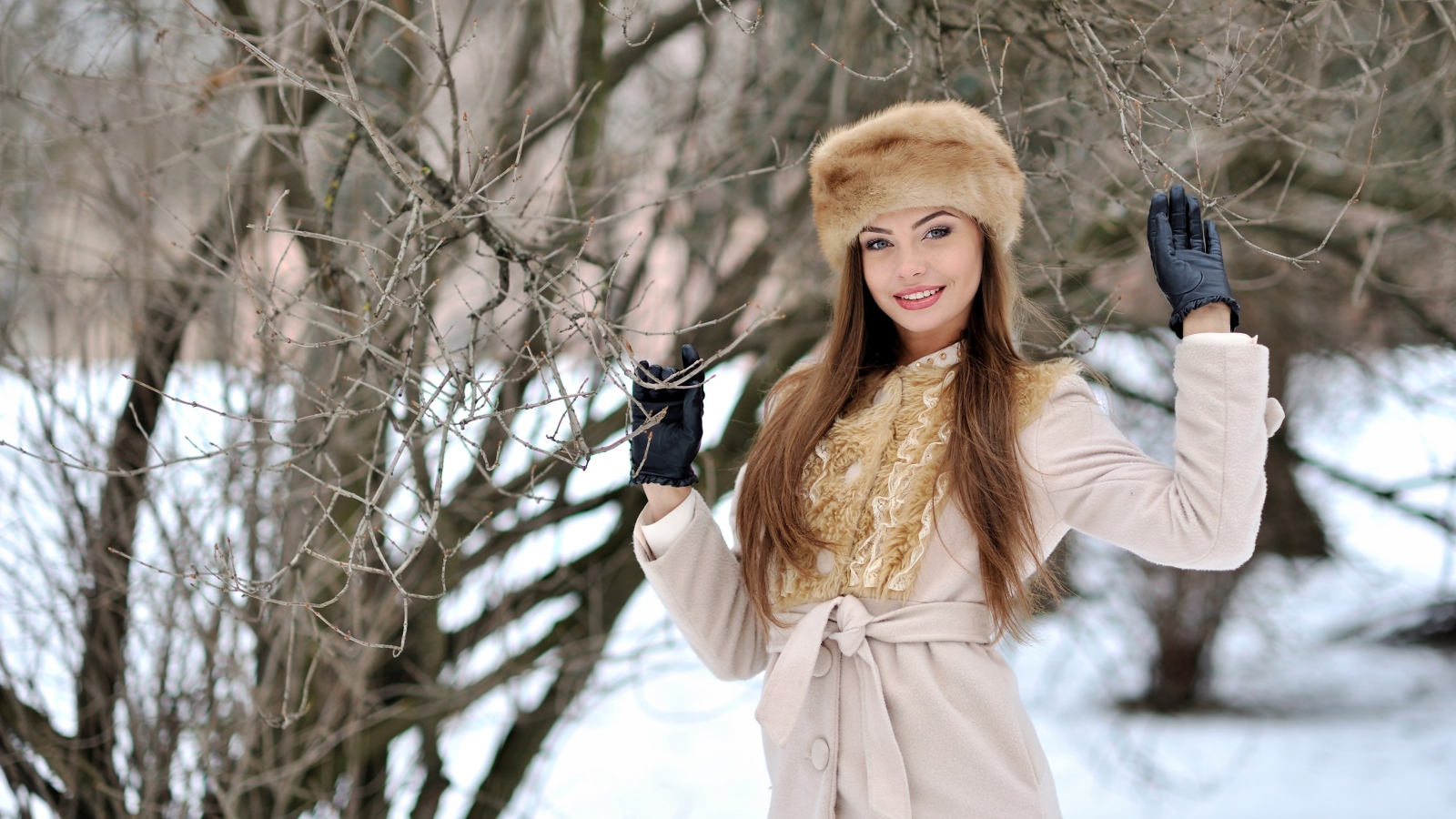 Красивая улыбающаяся девушка в шапке у дерева зимой