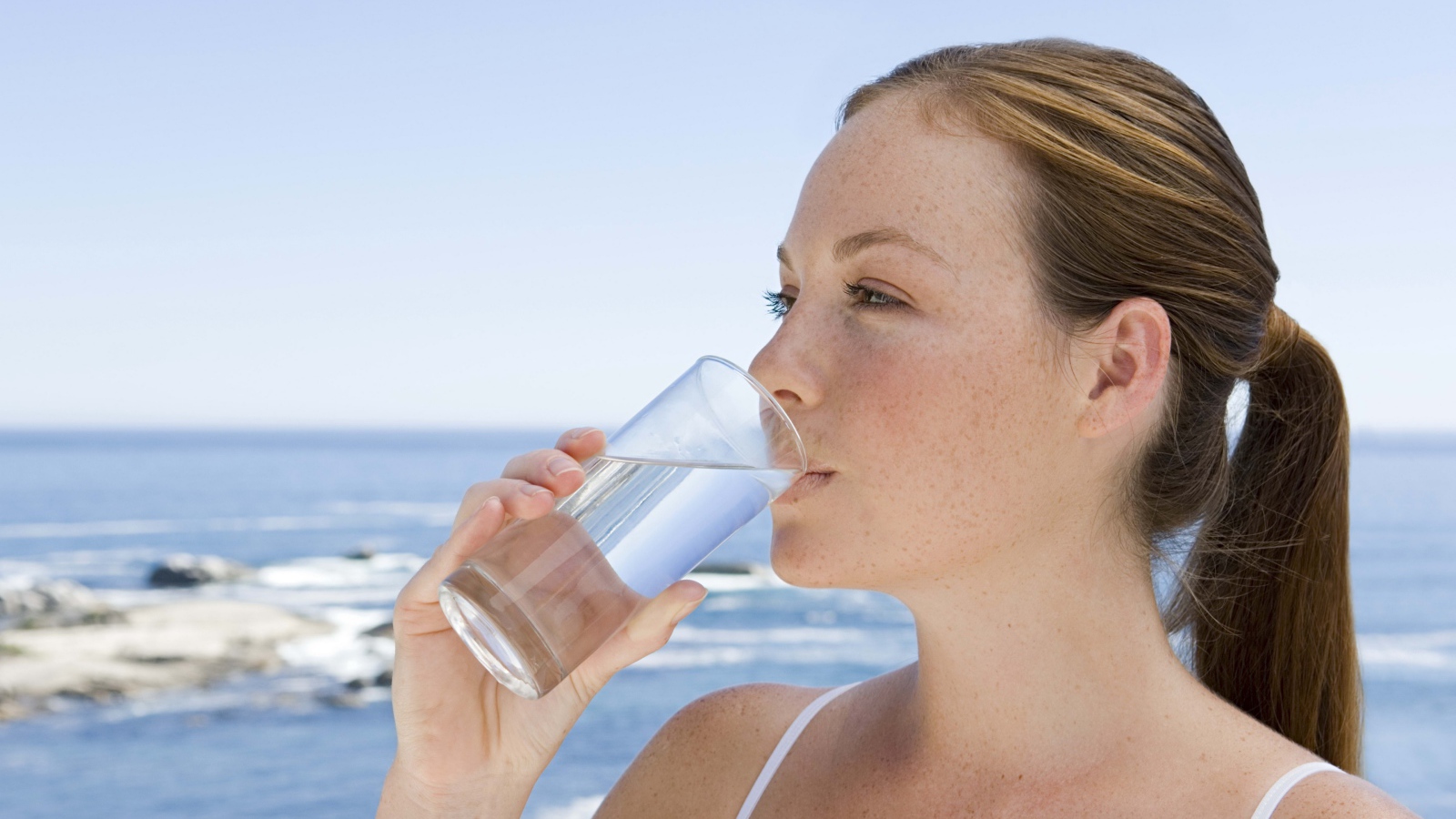 Девушка пьет воду со стакана на фоне моря