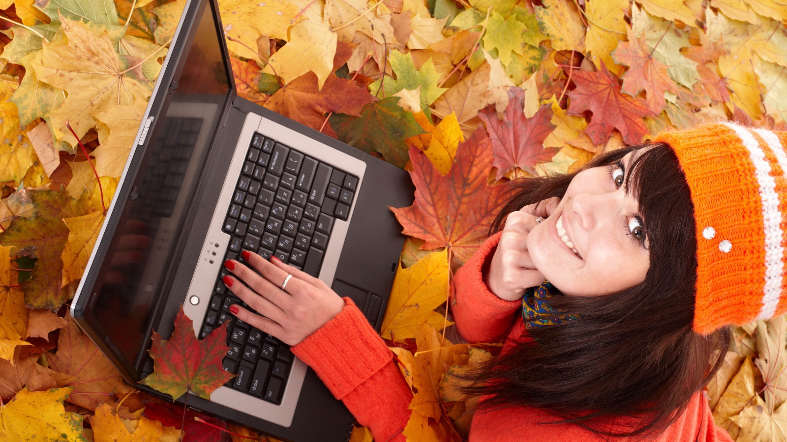 Девушка лежит на сухой опавшей листве с ноутбуком осенью